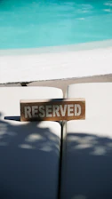 A wooden sign reading reserved on lounge chairs by pool.