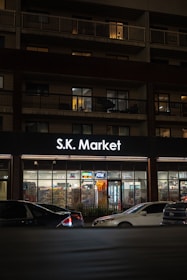 S.k. market store illuminated at night with cars outside