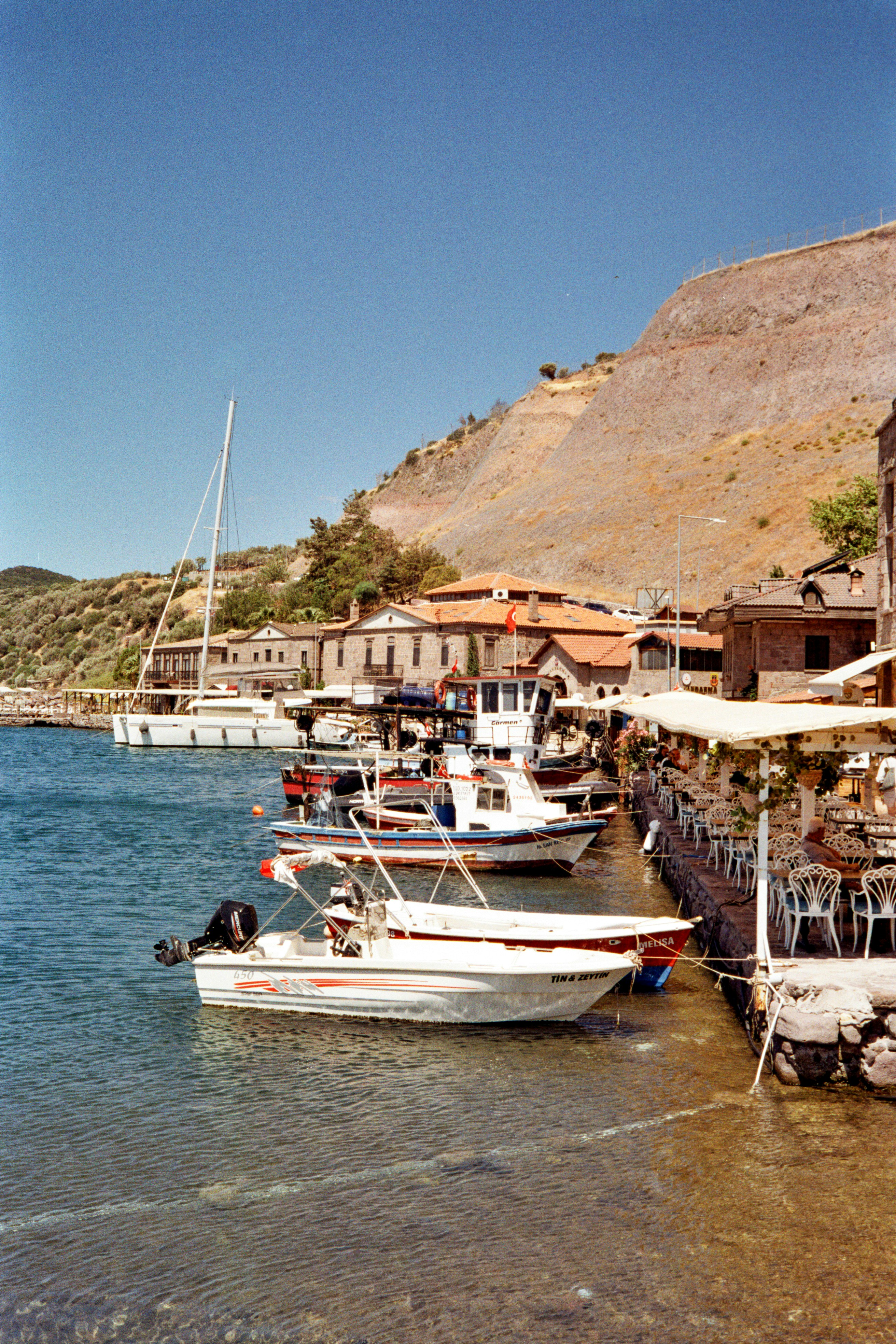 Boats docked in a coastal town with buildings and hills.