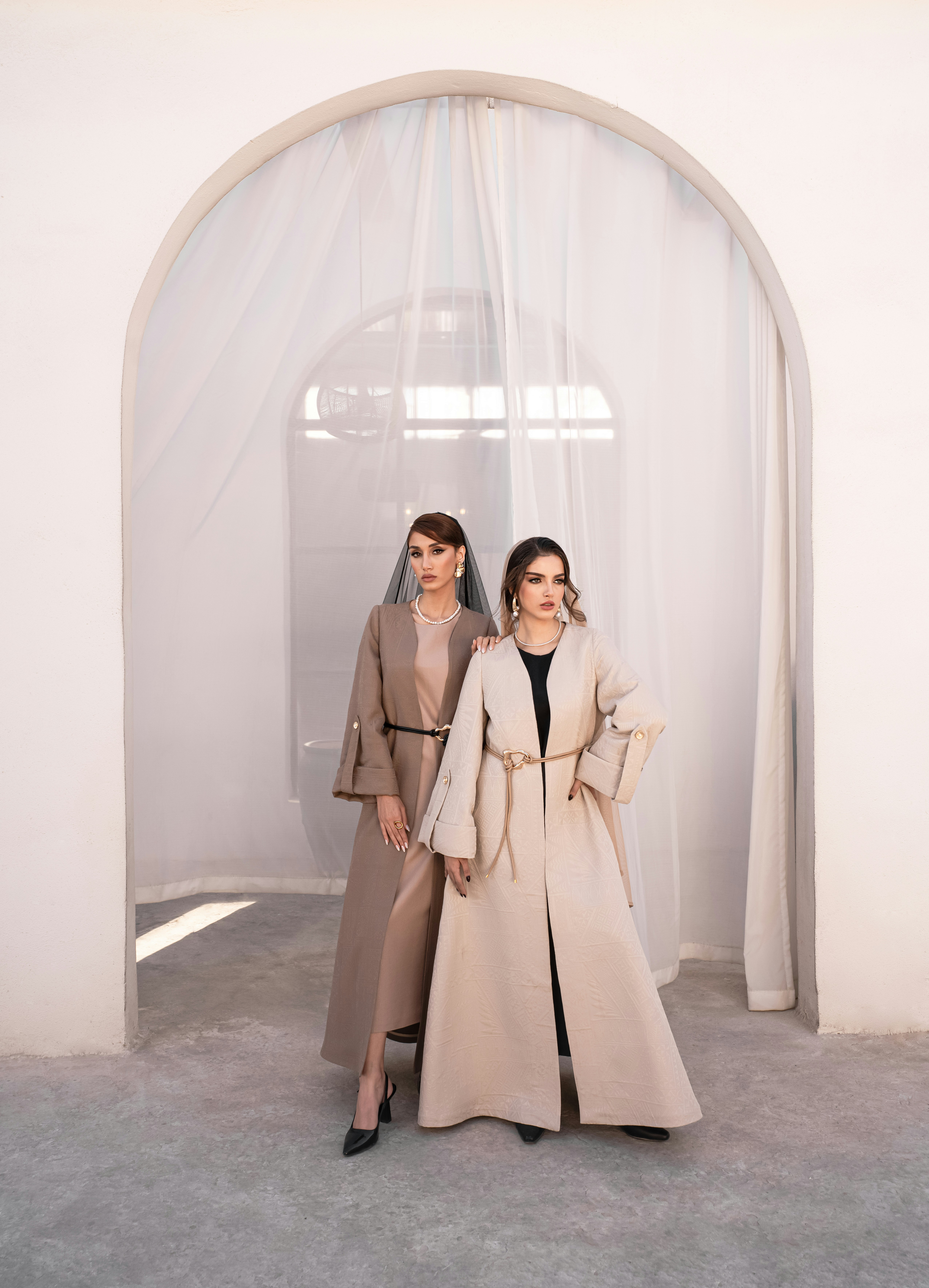 Two women in elegant abayas standing indoors.