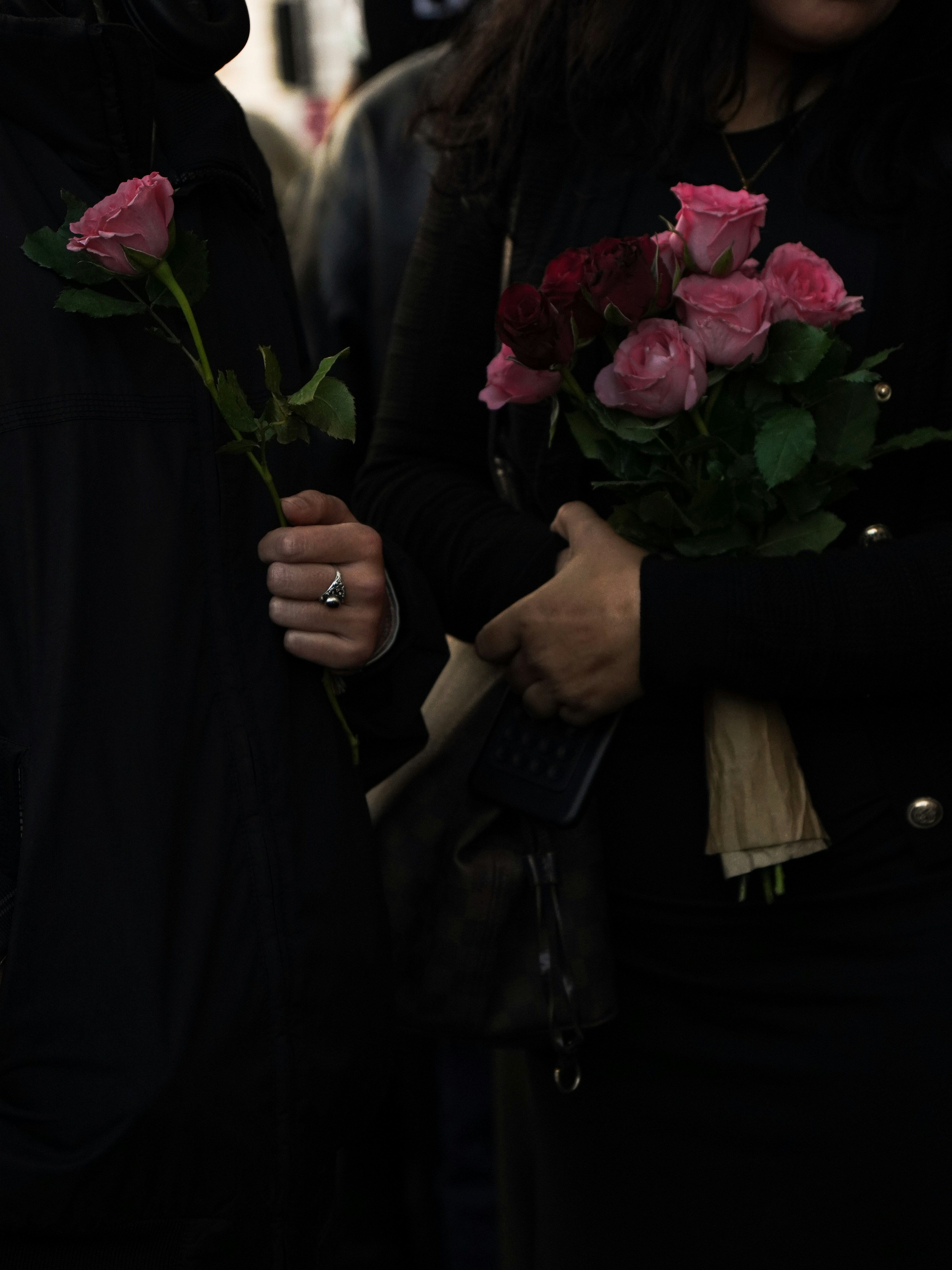 Two people holding pink roses, one a bouquet.