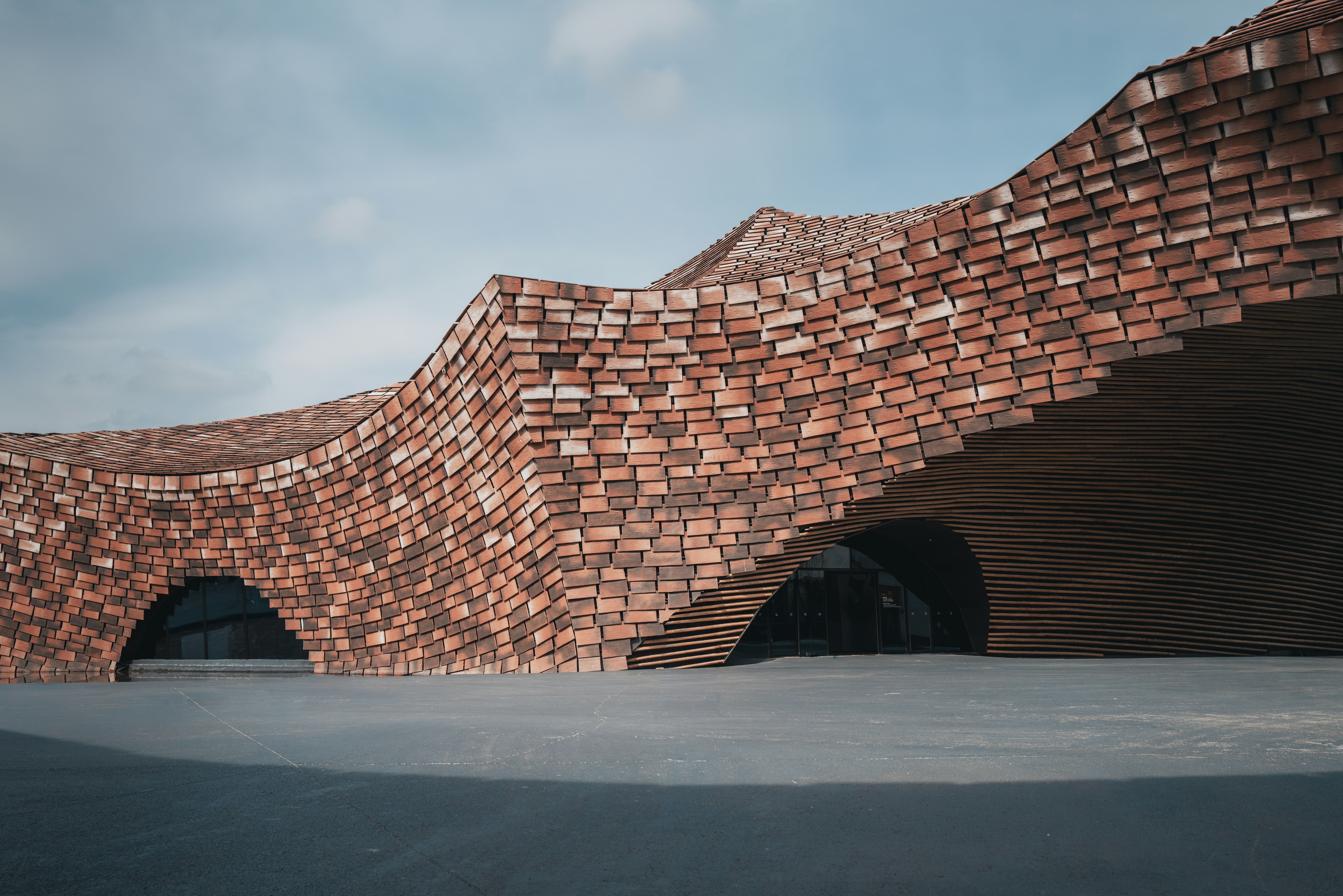 Curving brick structure with arched openings under sky