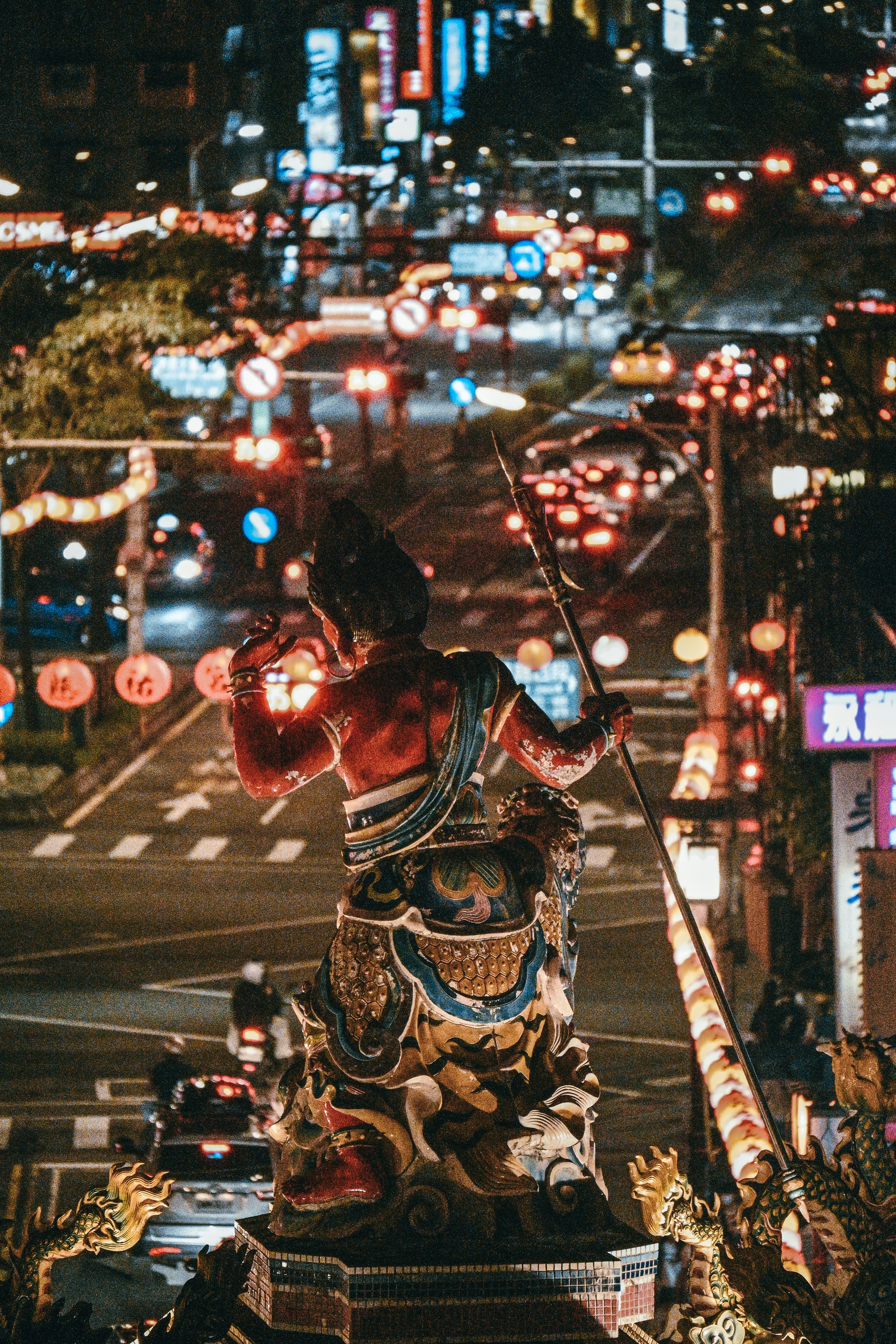 Ornate statue overlooks a bustling city street at night.
