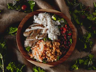 A wooden bowl filled with chicken, rice, and beans.