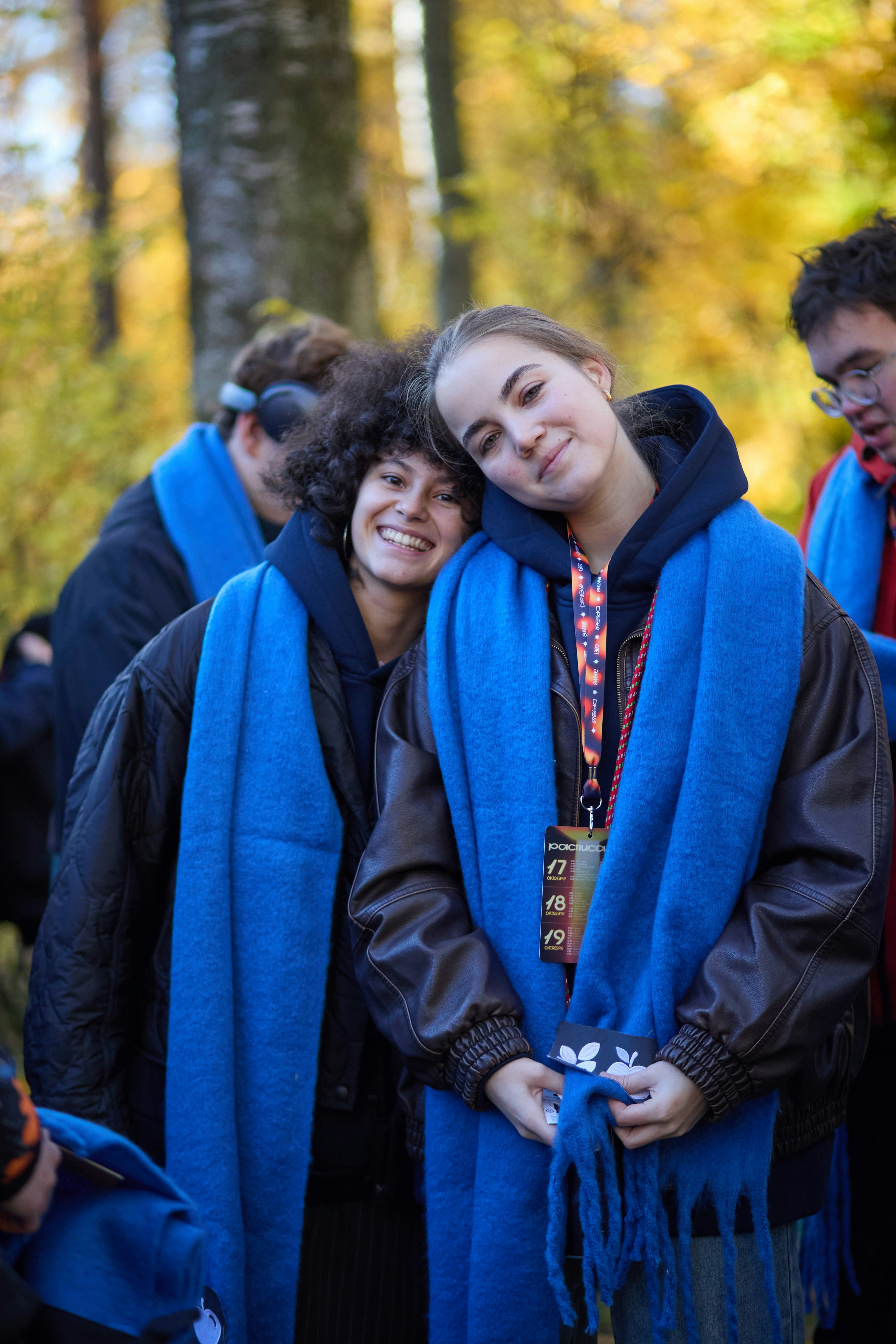 Two smiling young women wearing blue scarves outdoors.