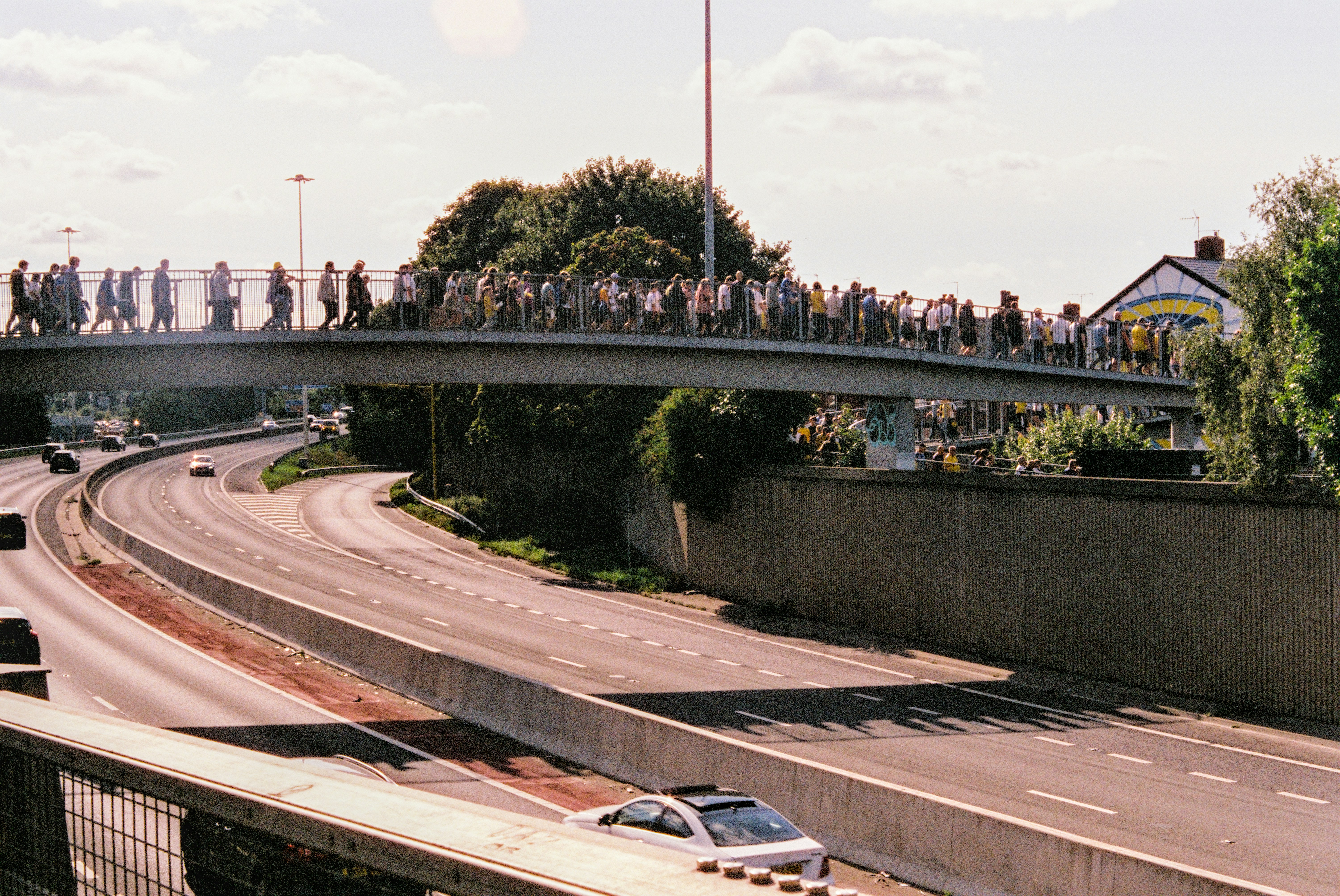 Crowd of people walking on a pedestrian bridge over highway.