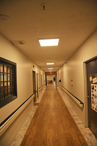 Long hospital hallway with wooden floor and doors.