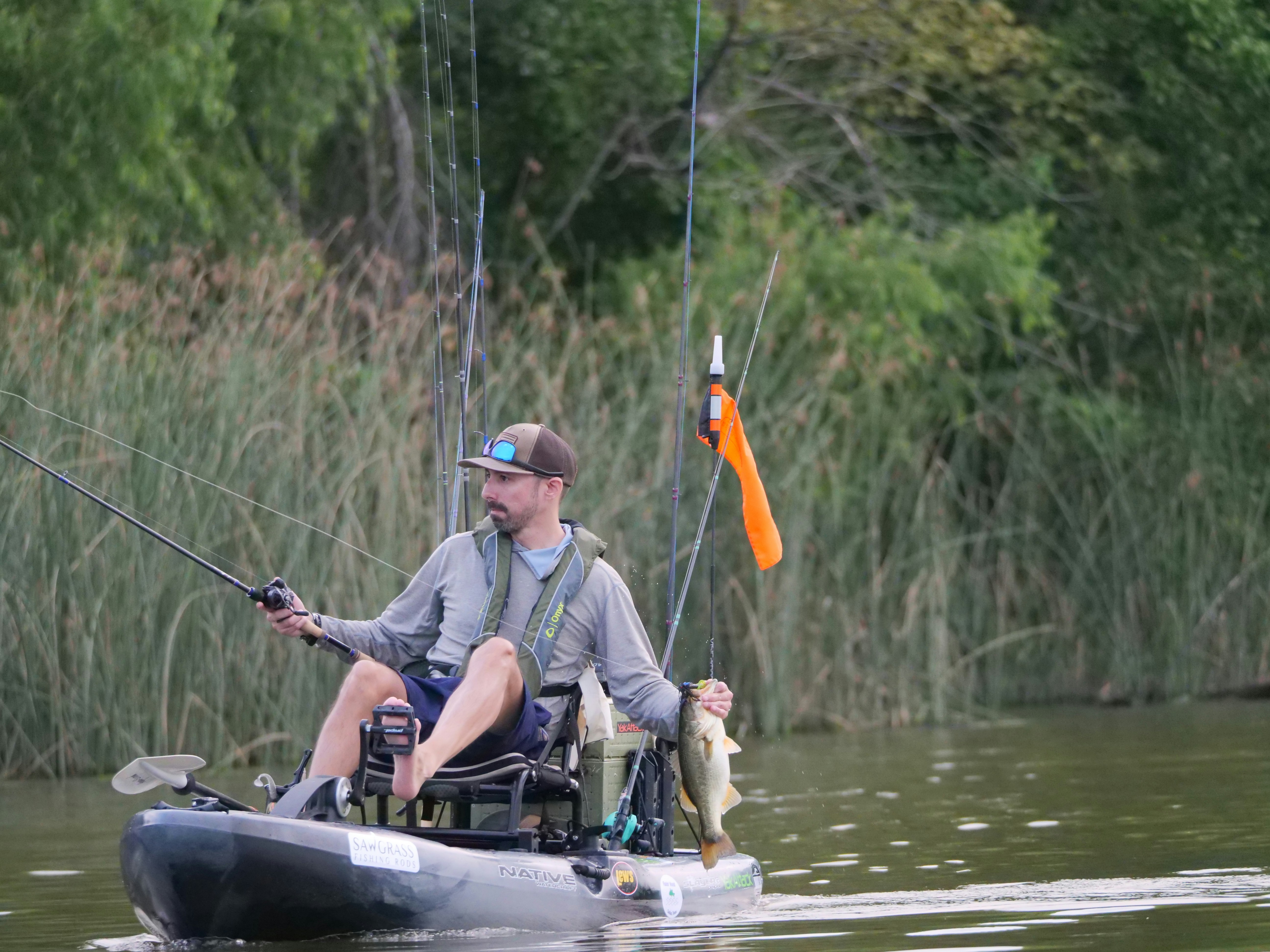Man fishing from kayak, holding a caught fish.