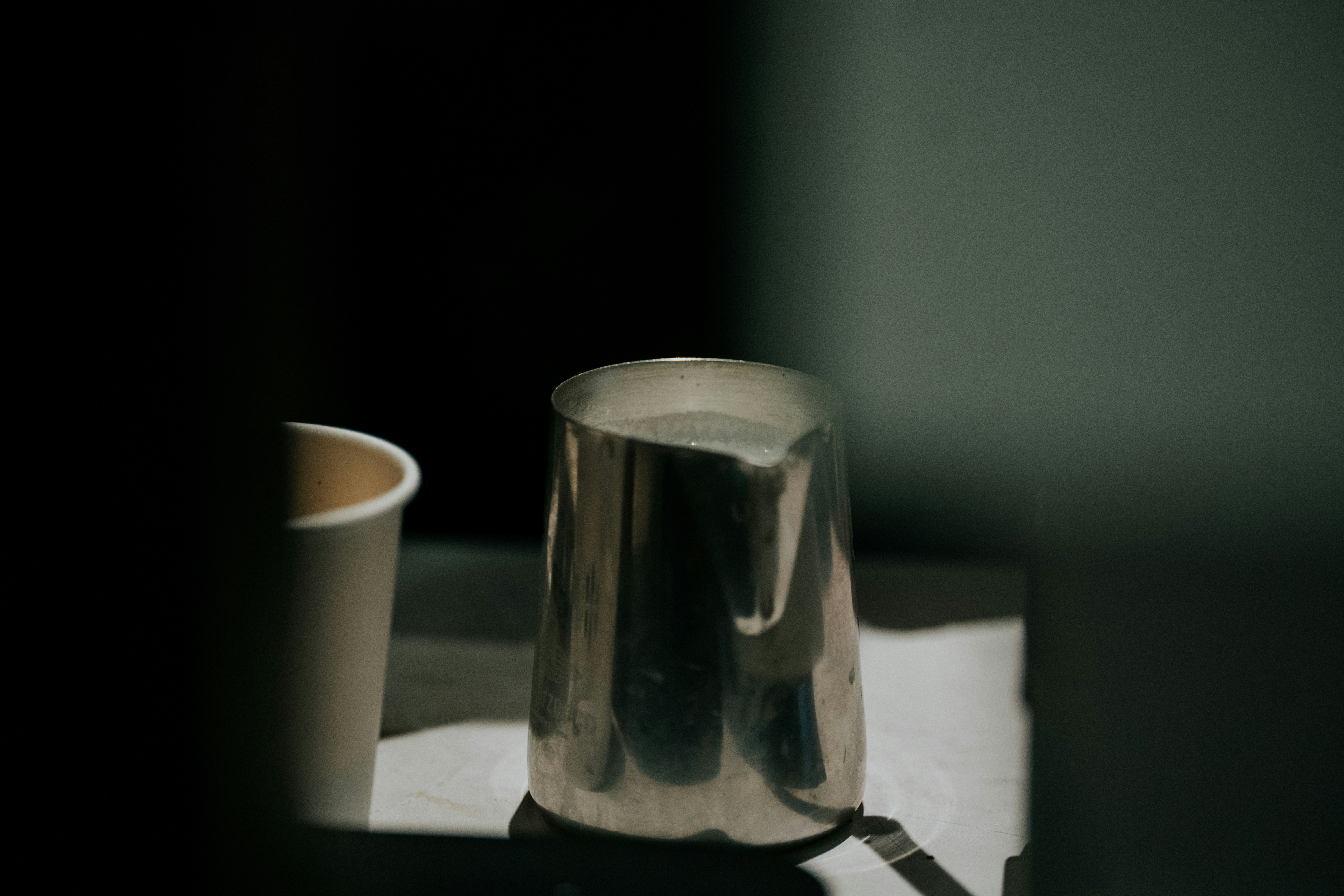 Metal pitcher and paper cup on tray.