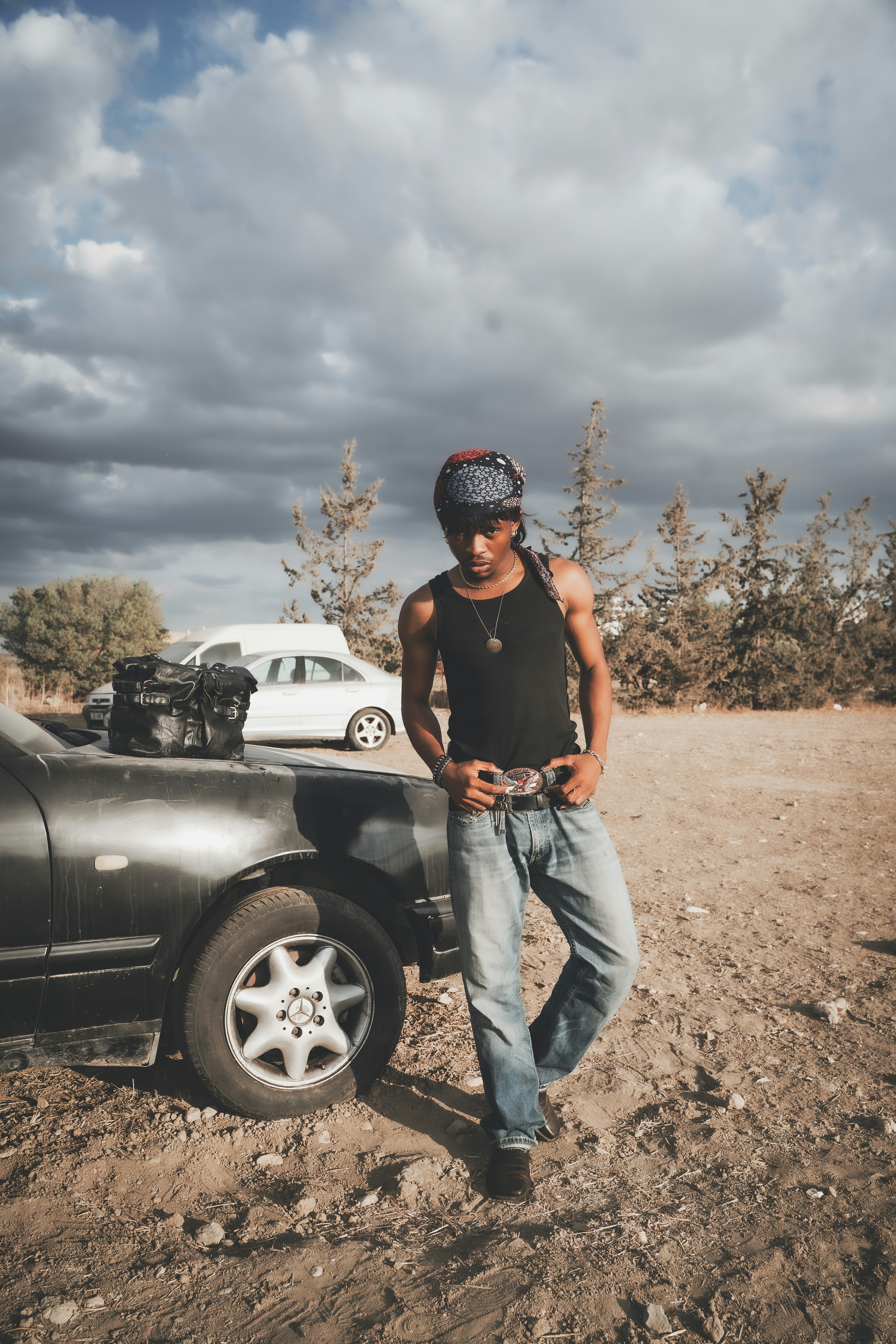 Mann in Bandana und Jeans lehnt sich an das Auto