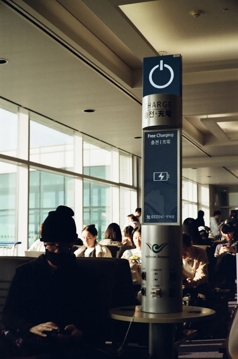 Travellers sitting by the window of an airport terminal next to a phone charging station