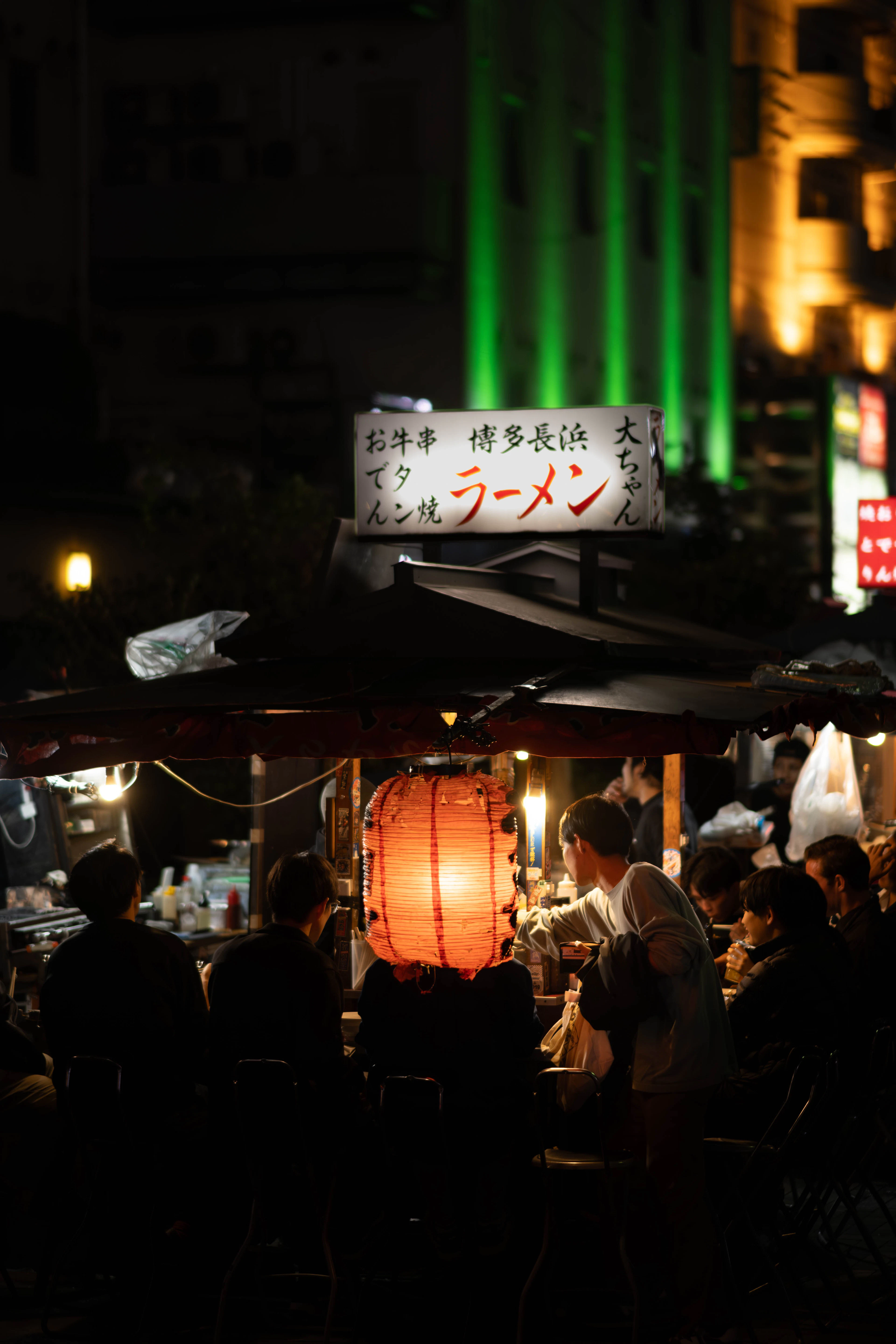 A Hakata Nagahama ramen yatai in Nakasu after dark, its red paper lantern lit above a crowded counter of late diners