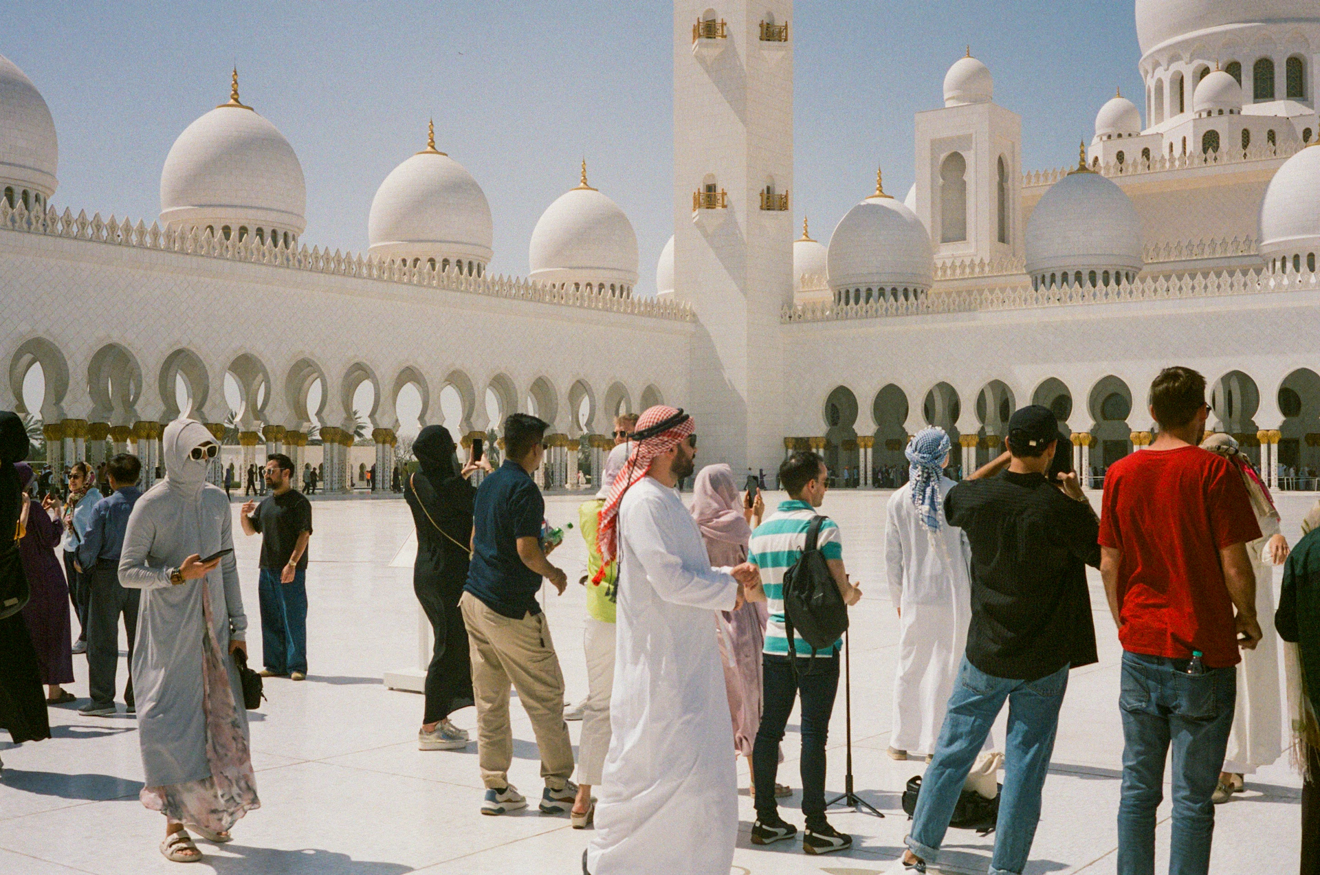 Tourists gather in a courtyard of a white mosque.