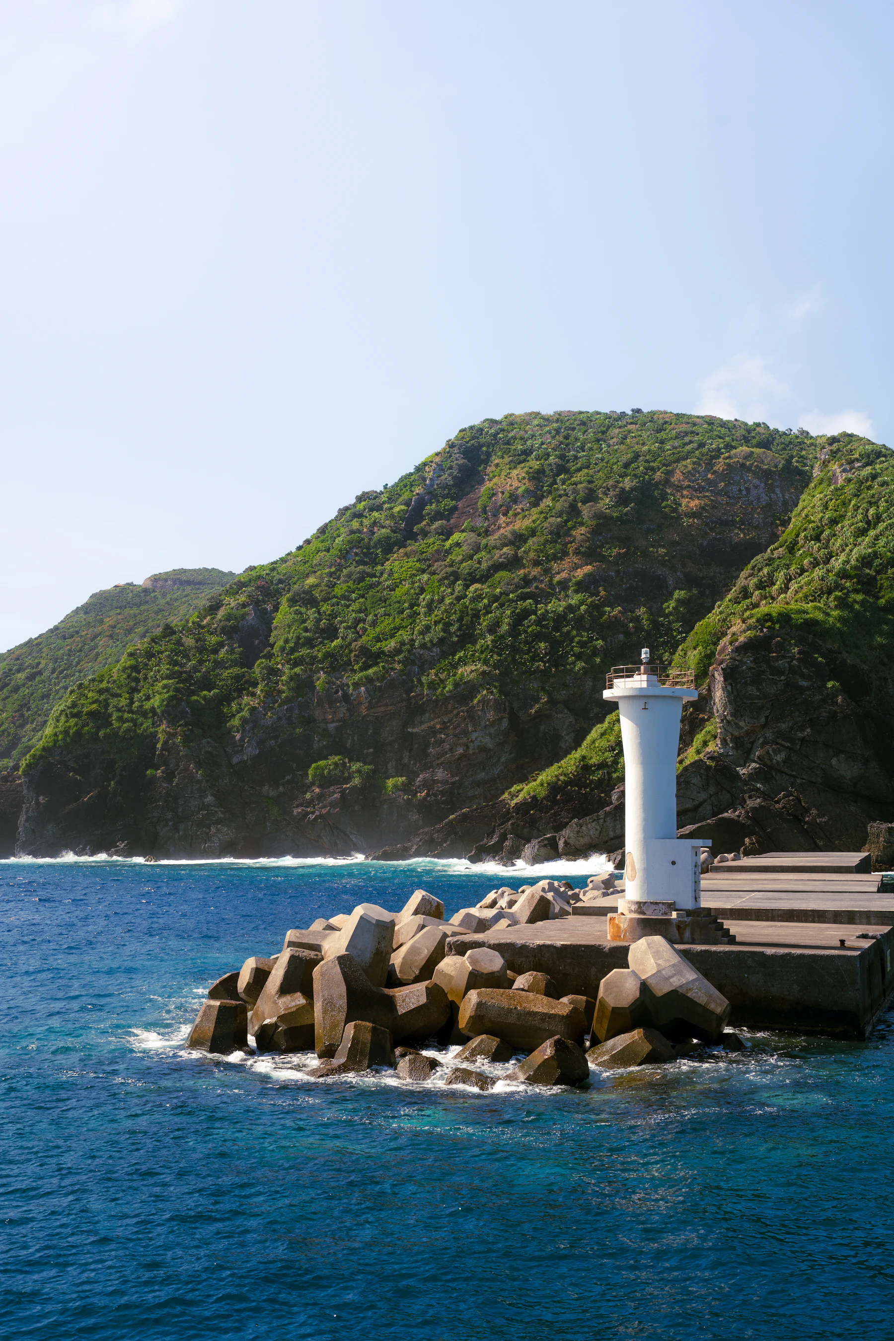 Weißer Leuchtturm vor grünen Felsen und tiefblauem Meer auf Okinawa
