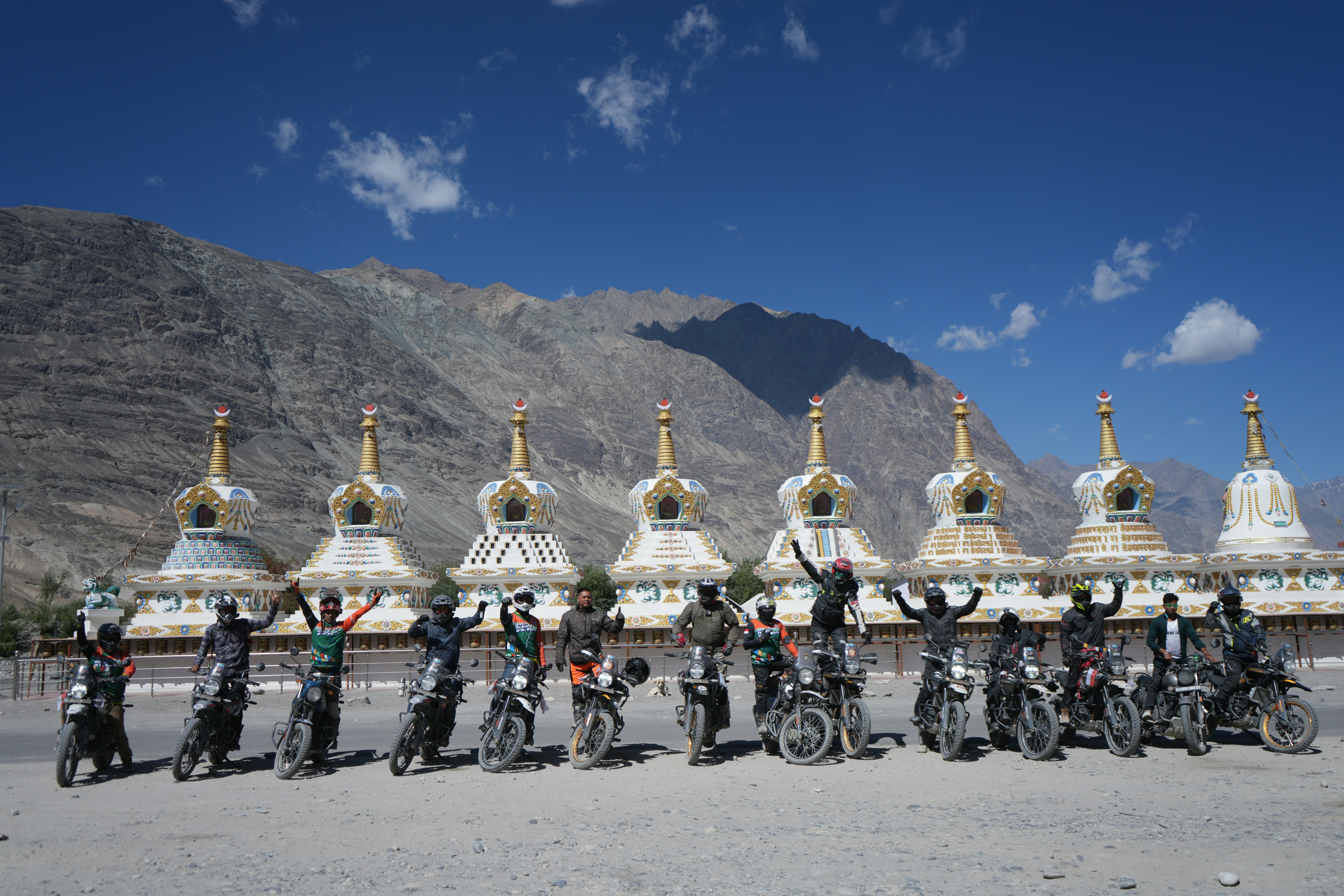 Group of motorcyclists posing with stupas and mountains