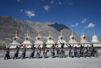 Group of motorcyclists posing with stupas and mountains
