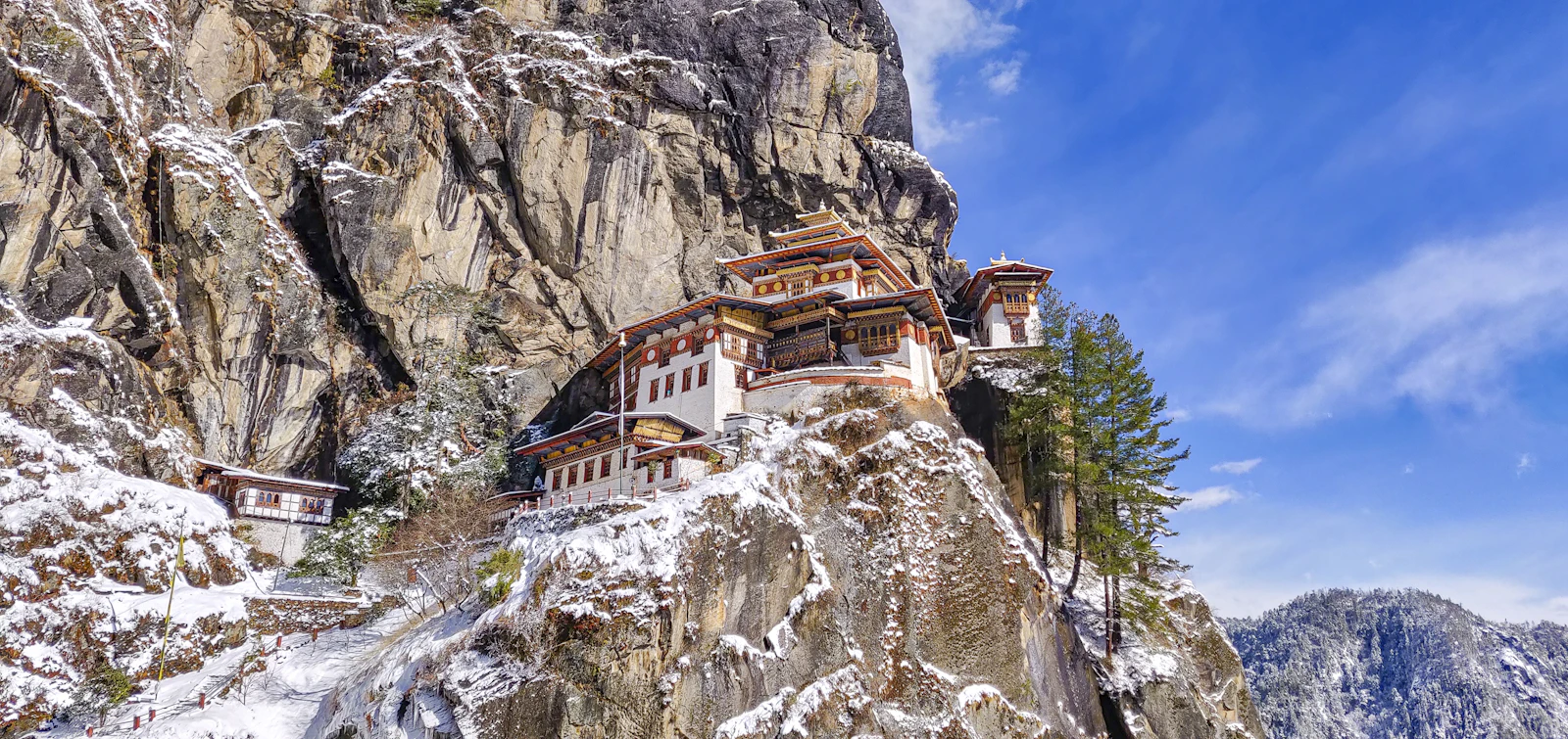 Taktsang monastery on its granite cliff above Paro after fresh snow, white walls bright against a hard blue sky