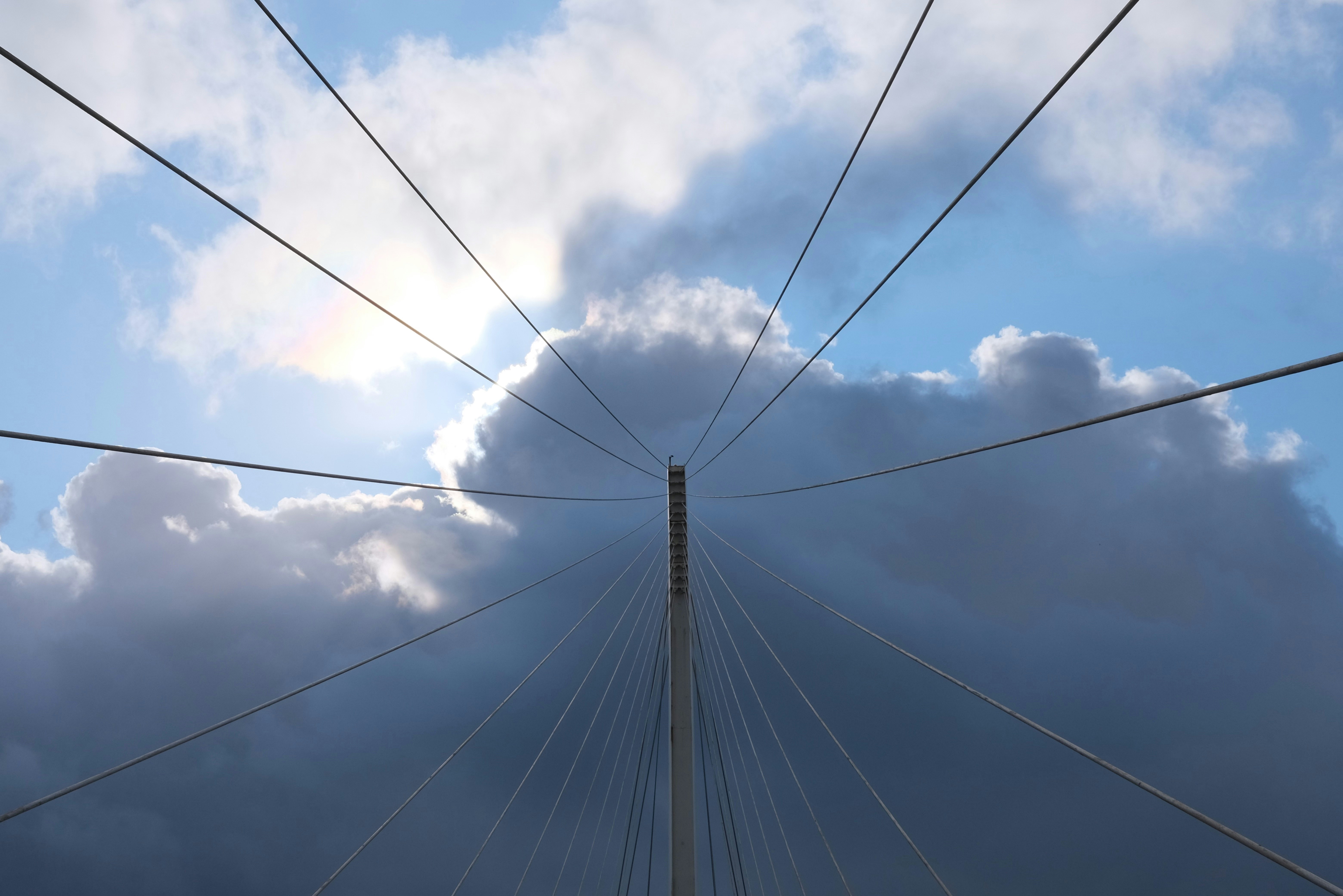 Sunlight breaks through dramatic clouds over bridge cables
