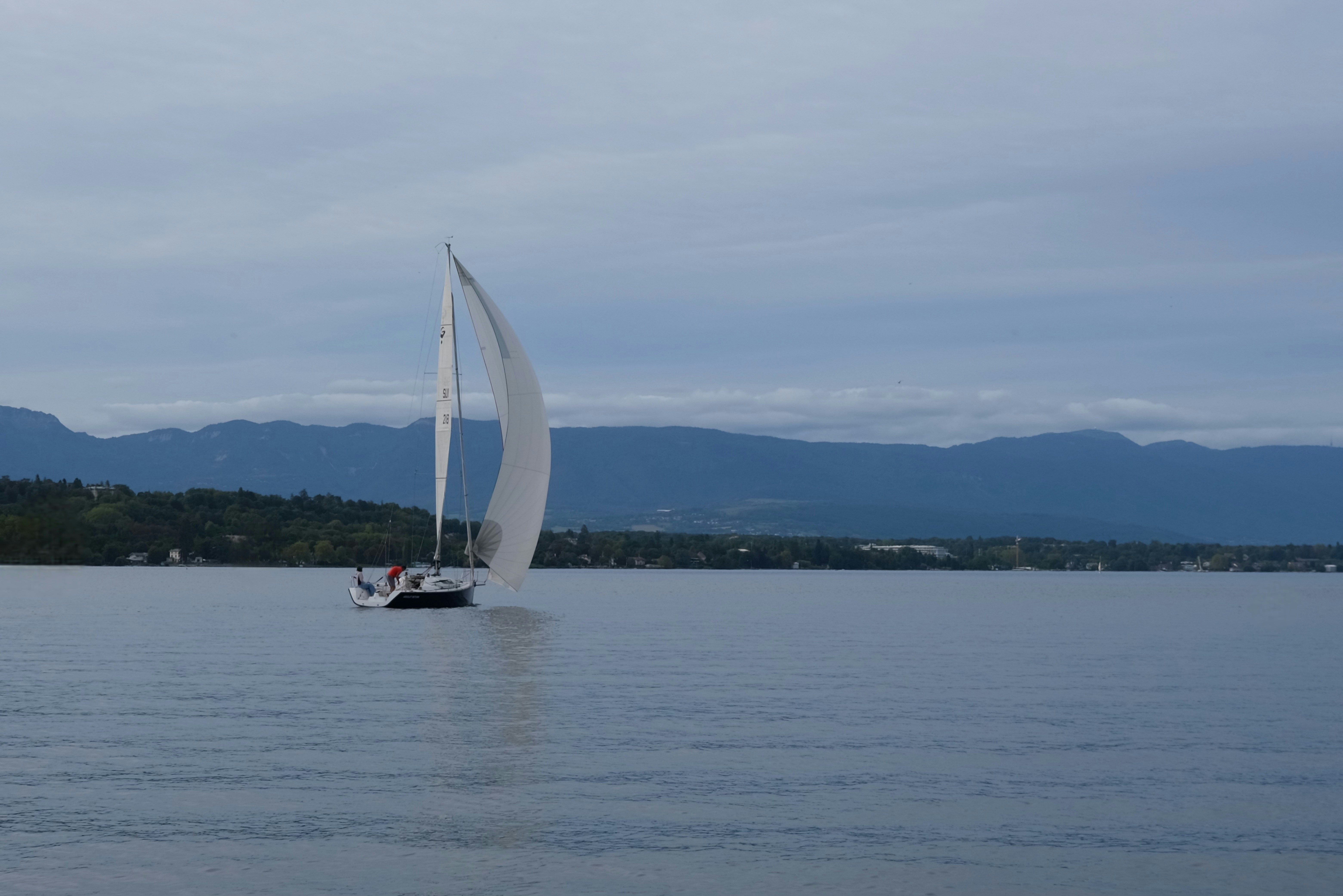 Sailboat glides across calm water near mountains.