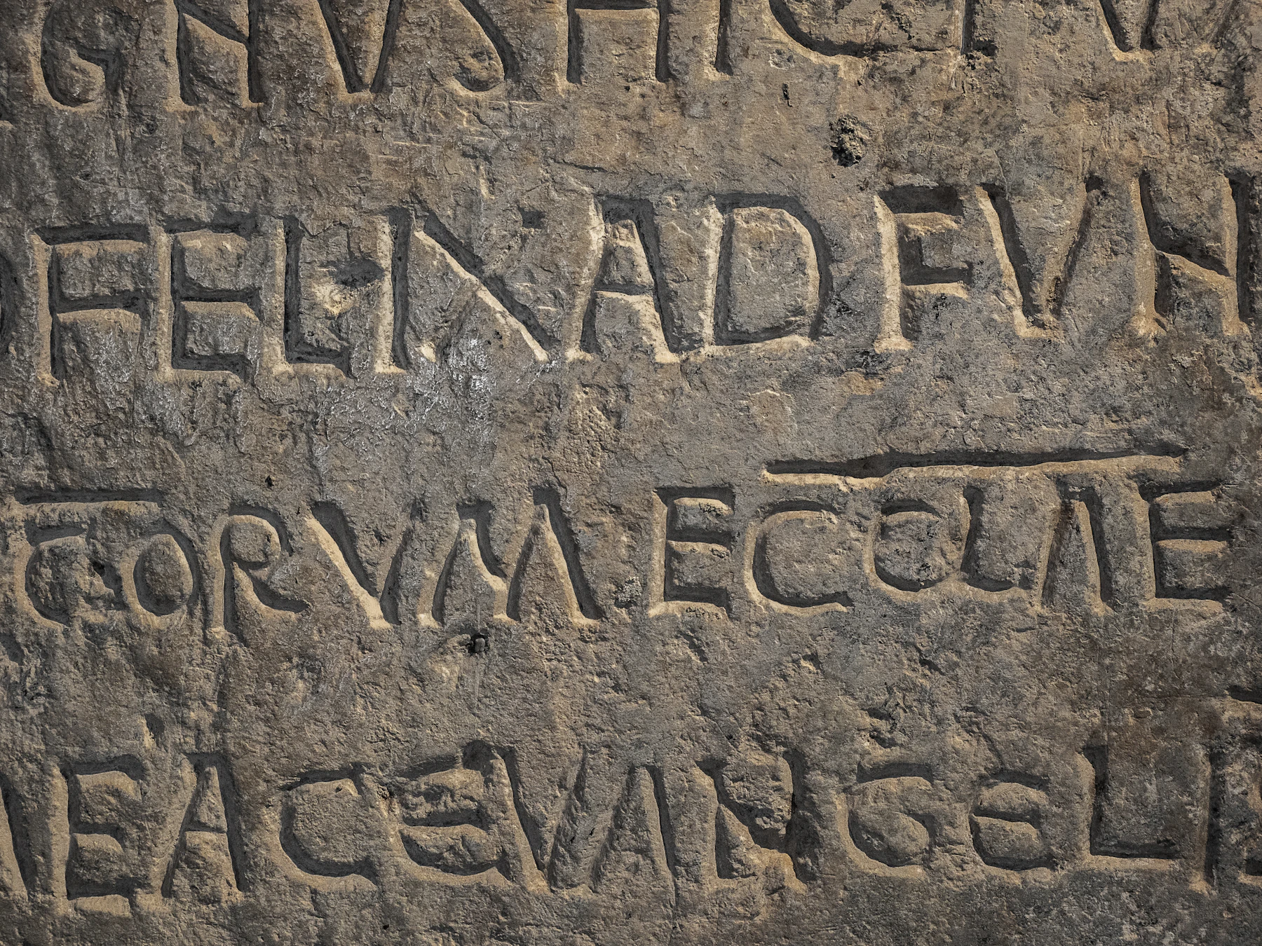Close-up of a weathered stone inscription whose letters are joined and abbreviated