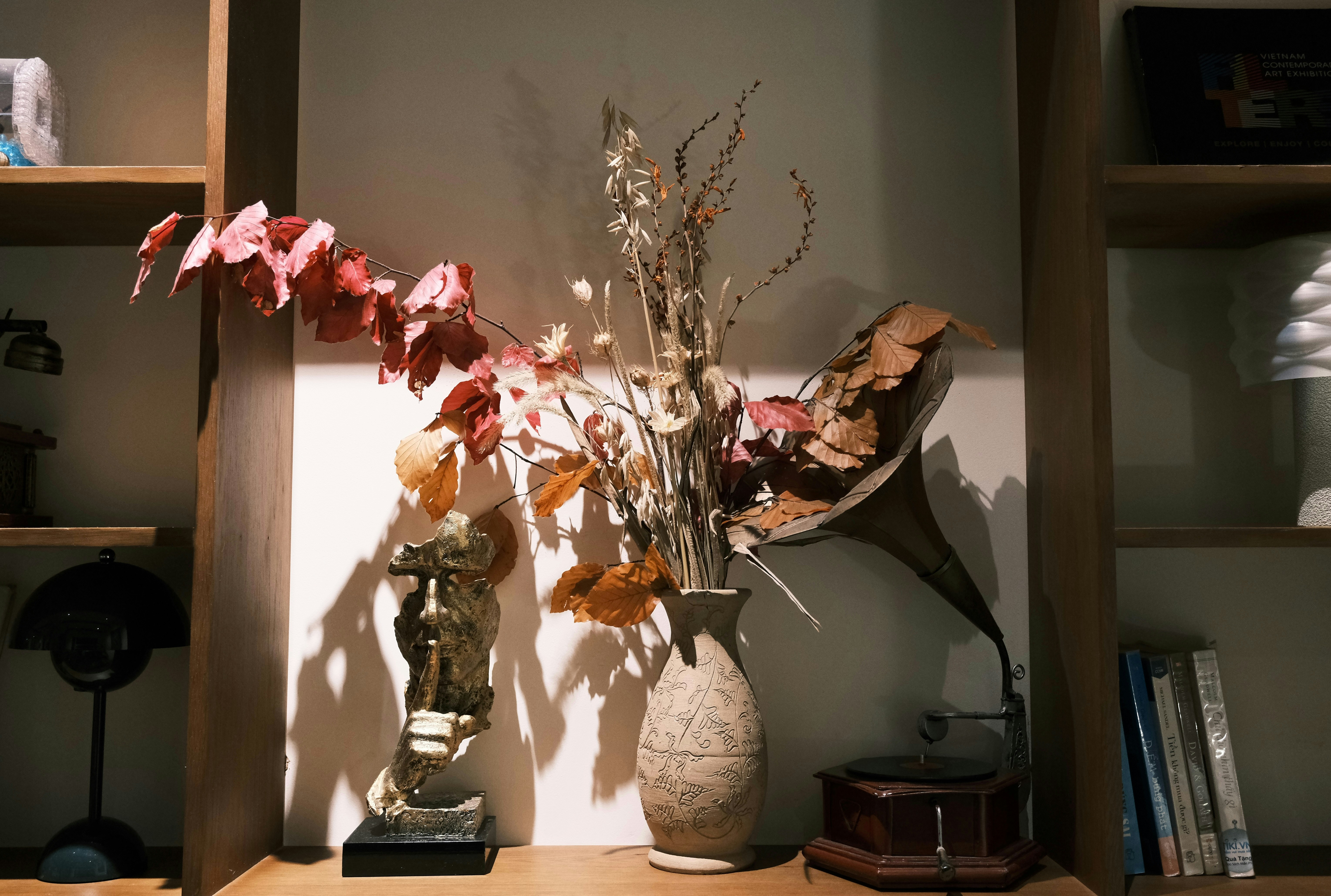 Dried flowers in vase with vintage gramophone and statue.