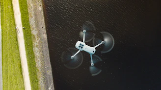 A white drone flies over dark water.