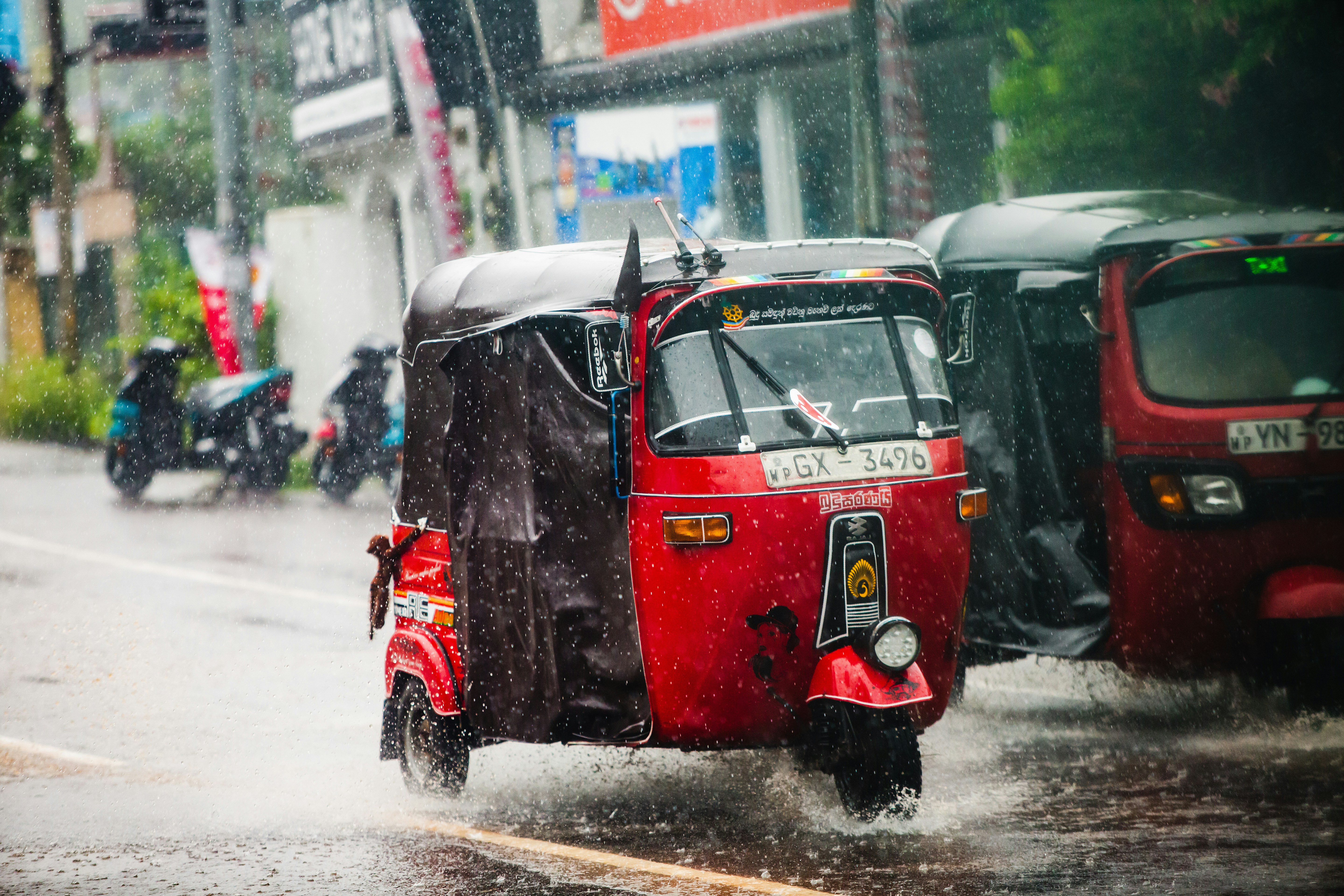 A red tuk-tuk drives through heavy rain.