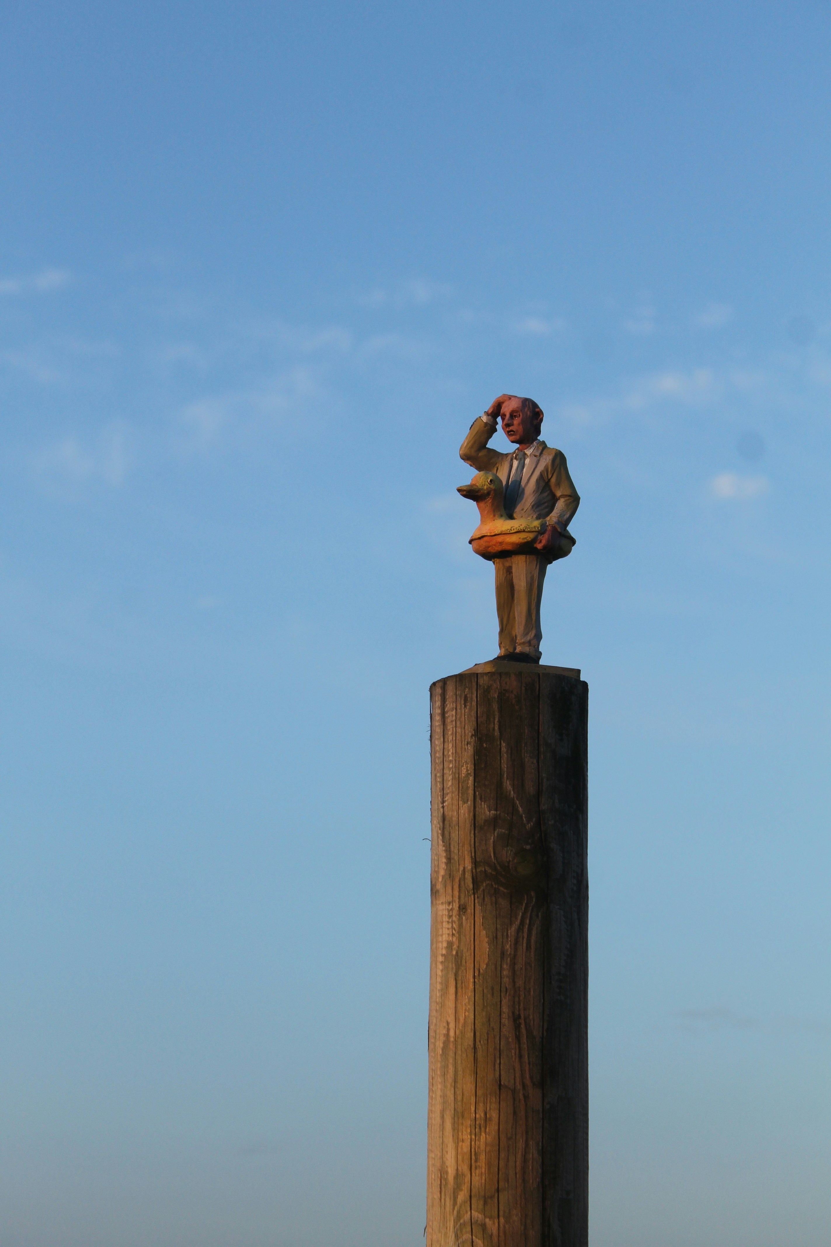 Statue of man looking out from wooden post.
