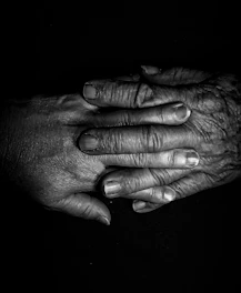 Close-up of intertwined elderly hands against black background.