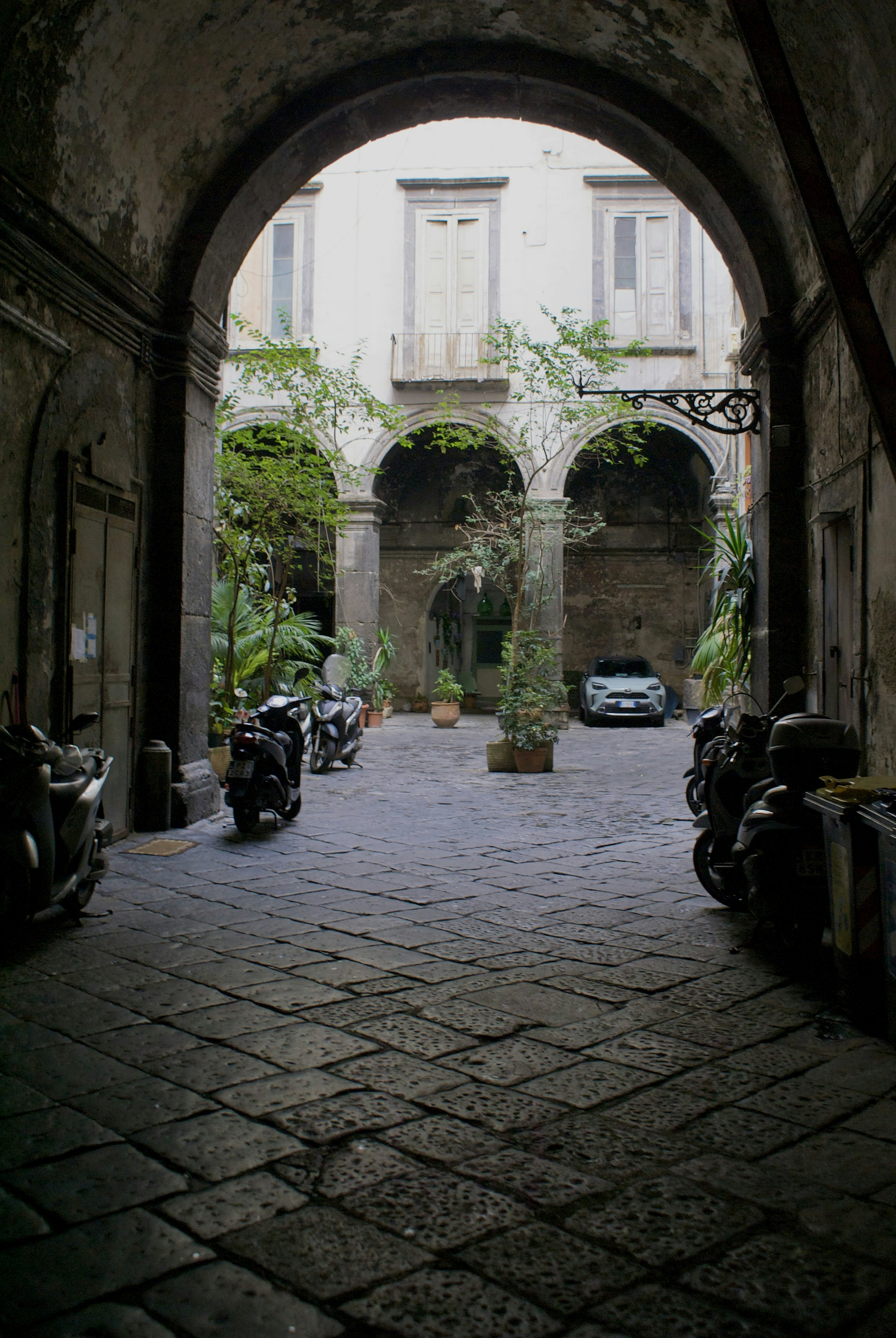 Courtyard with arches, scooters, and a car.