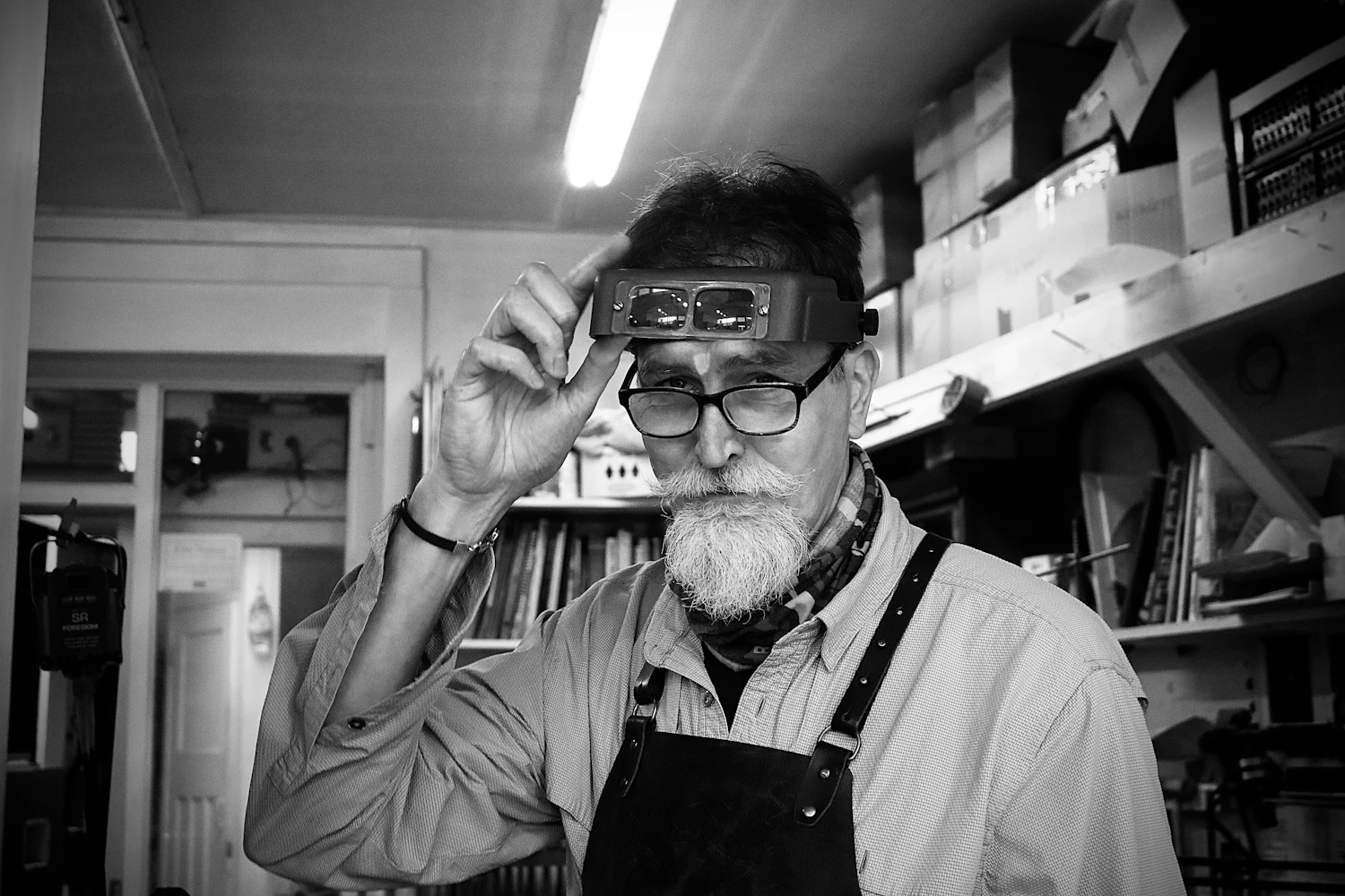 A watchmaker in an apron standing in the doorway of a lit workshop