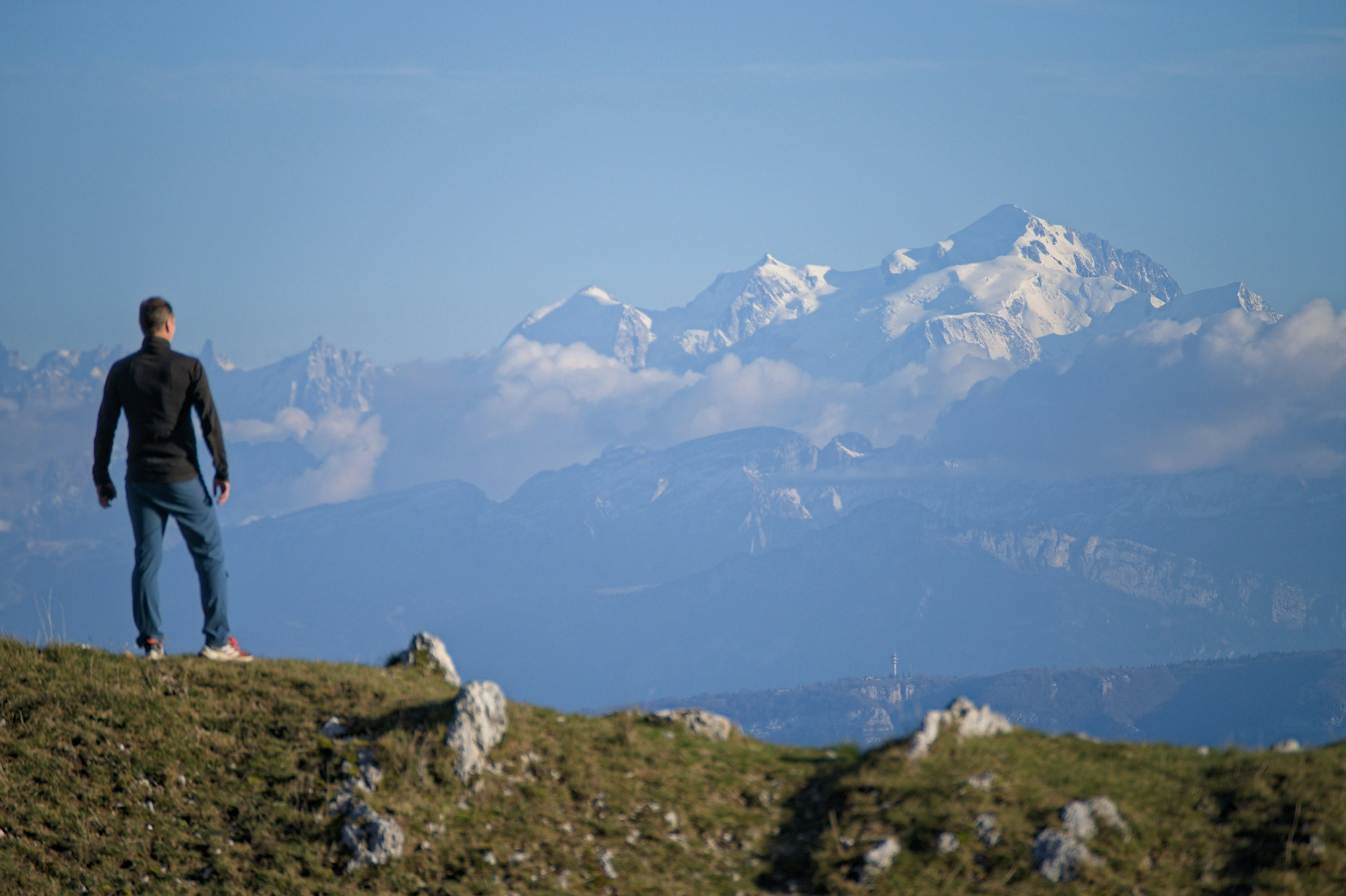 Man standing on a grassy hill overlooking mountains.