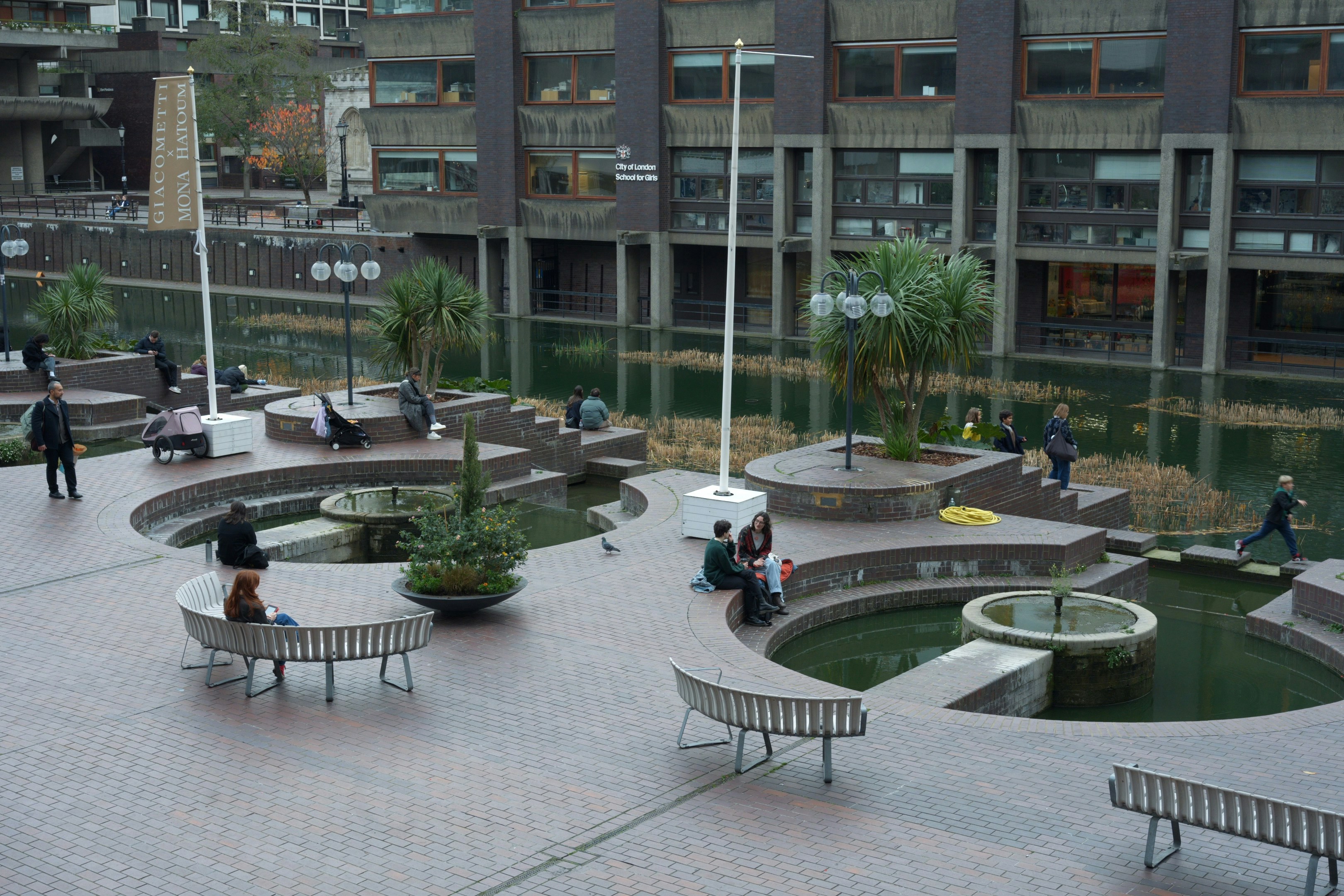People relax in a modern concrete plaza with water features.