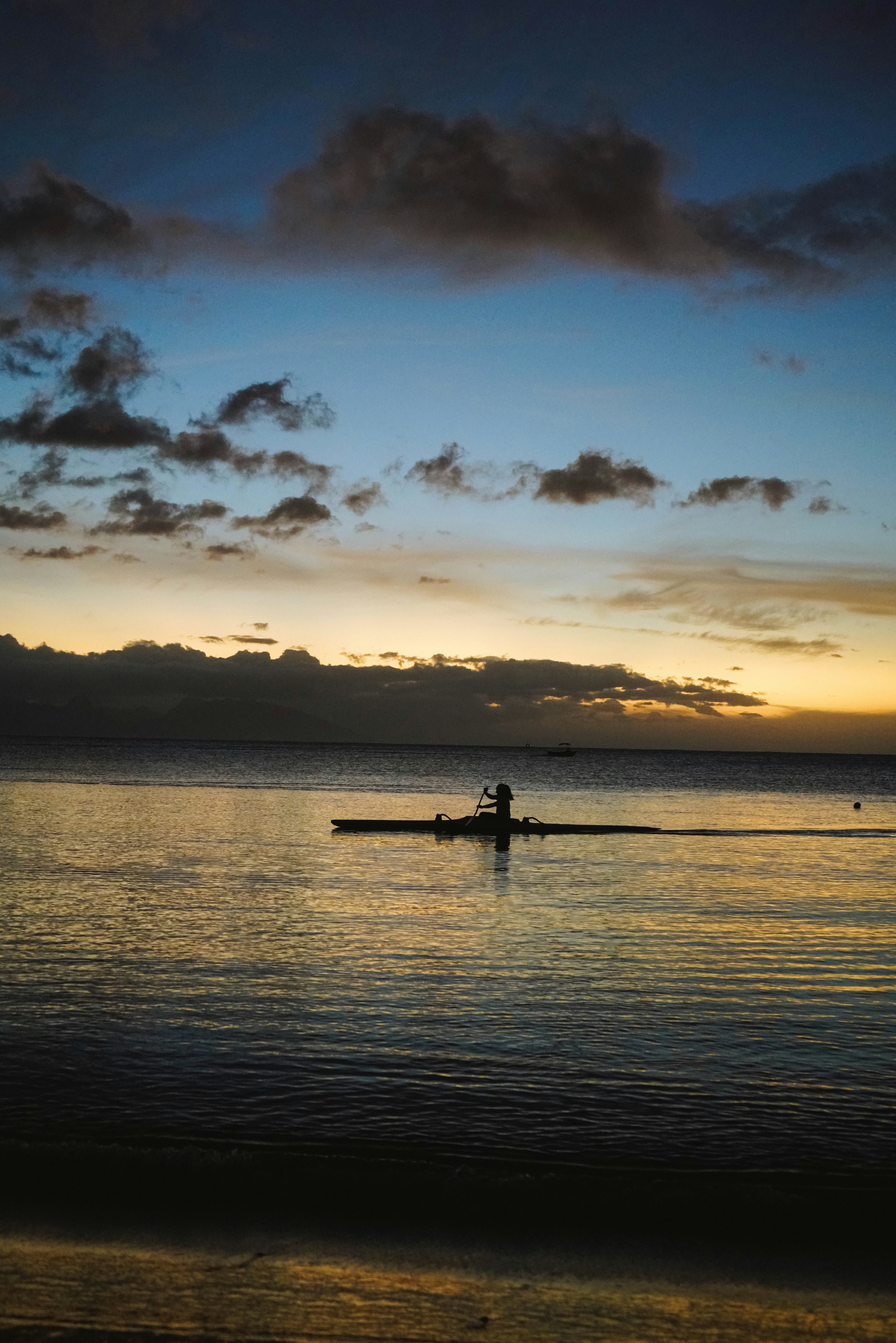 Un rameur solitaire sur un océan calme au coucher du soleil.