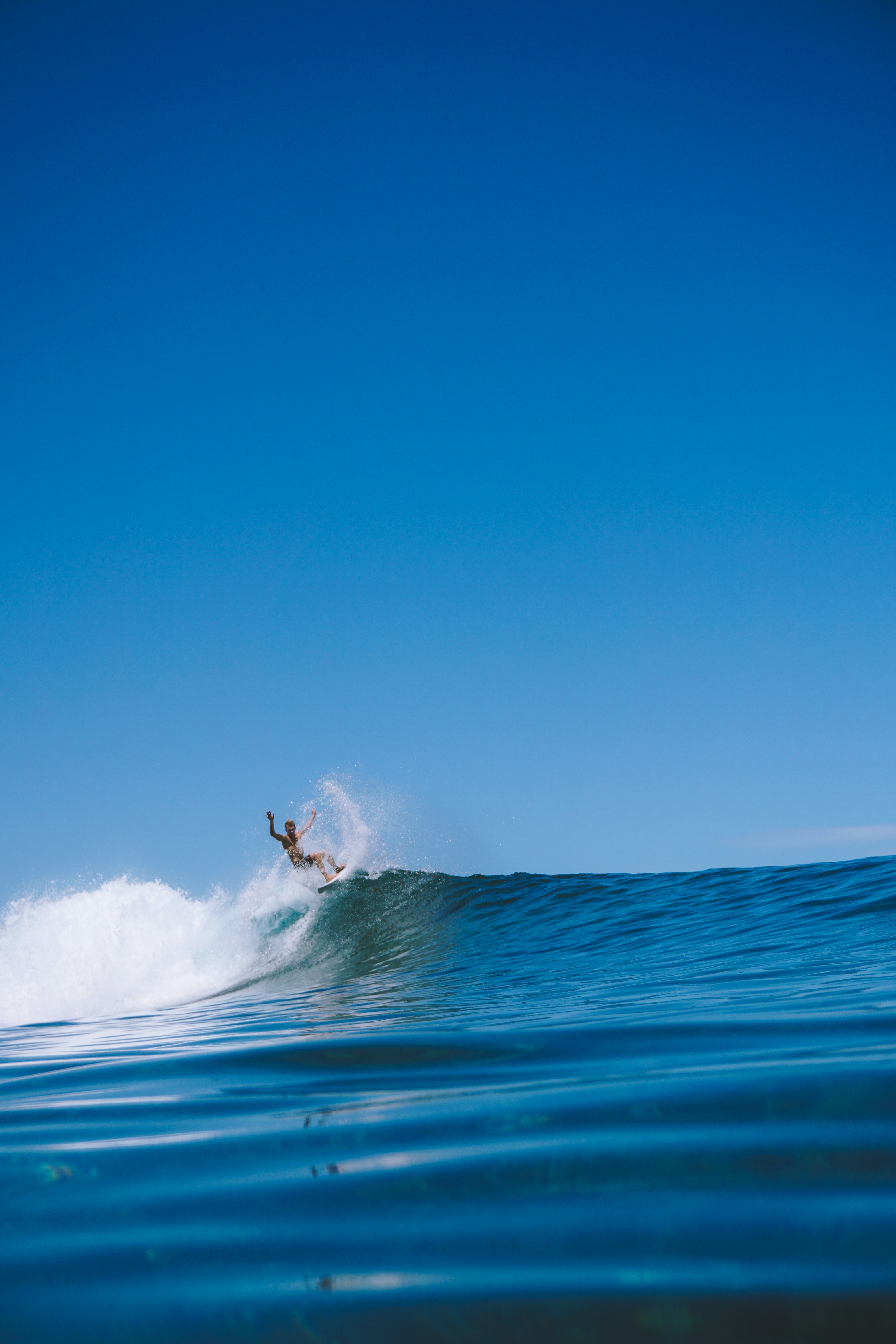Surfeur surfant sur une vague sous un ciel bleu clair.
