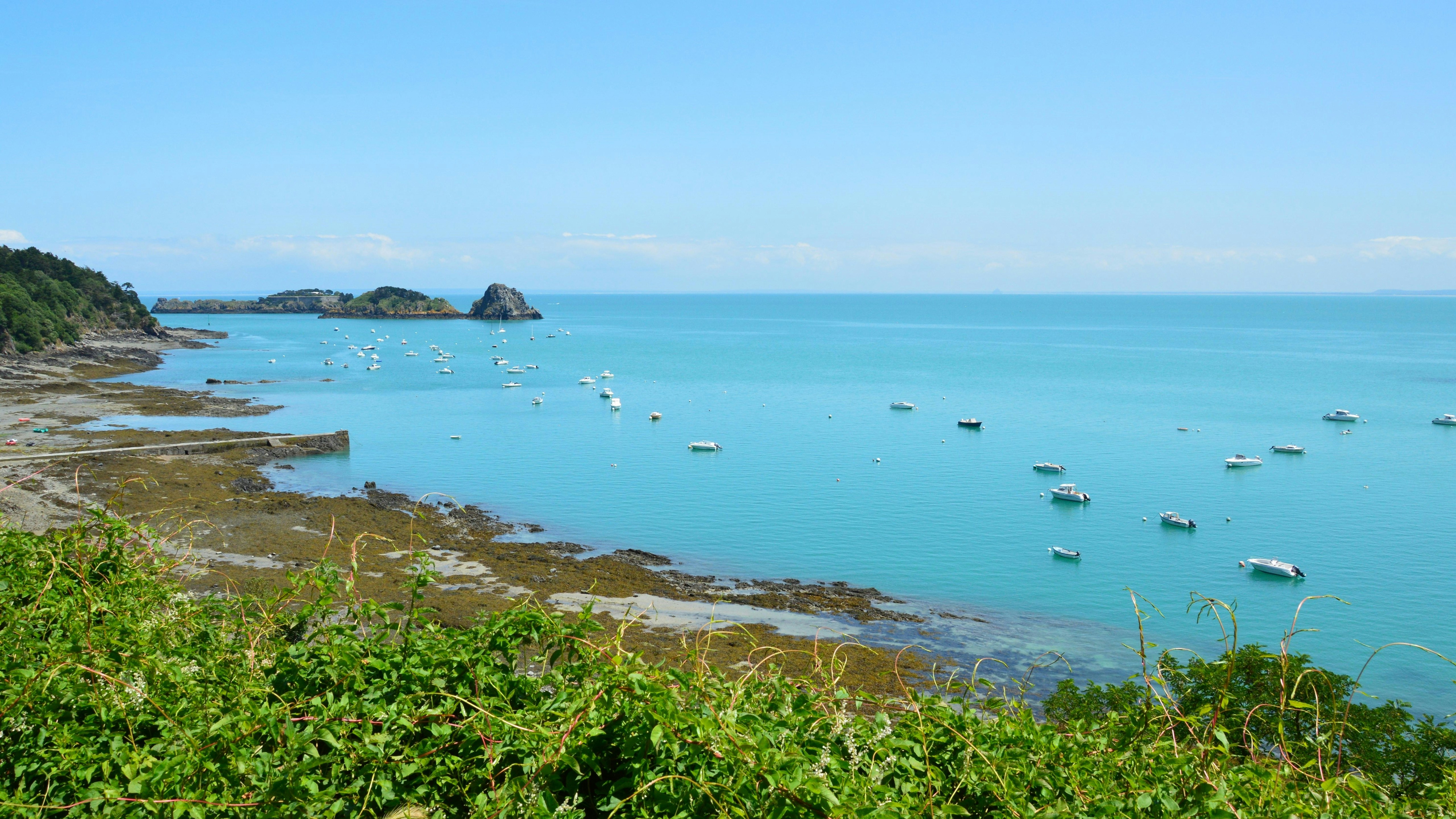 Boats anchored in a clear blue bay with rocky shore.