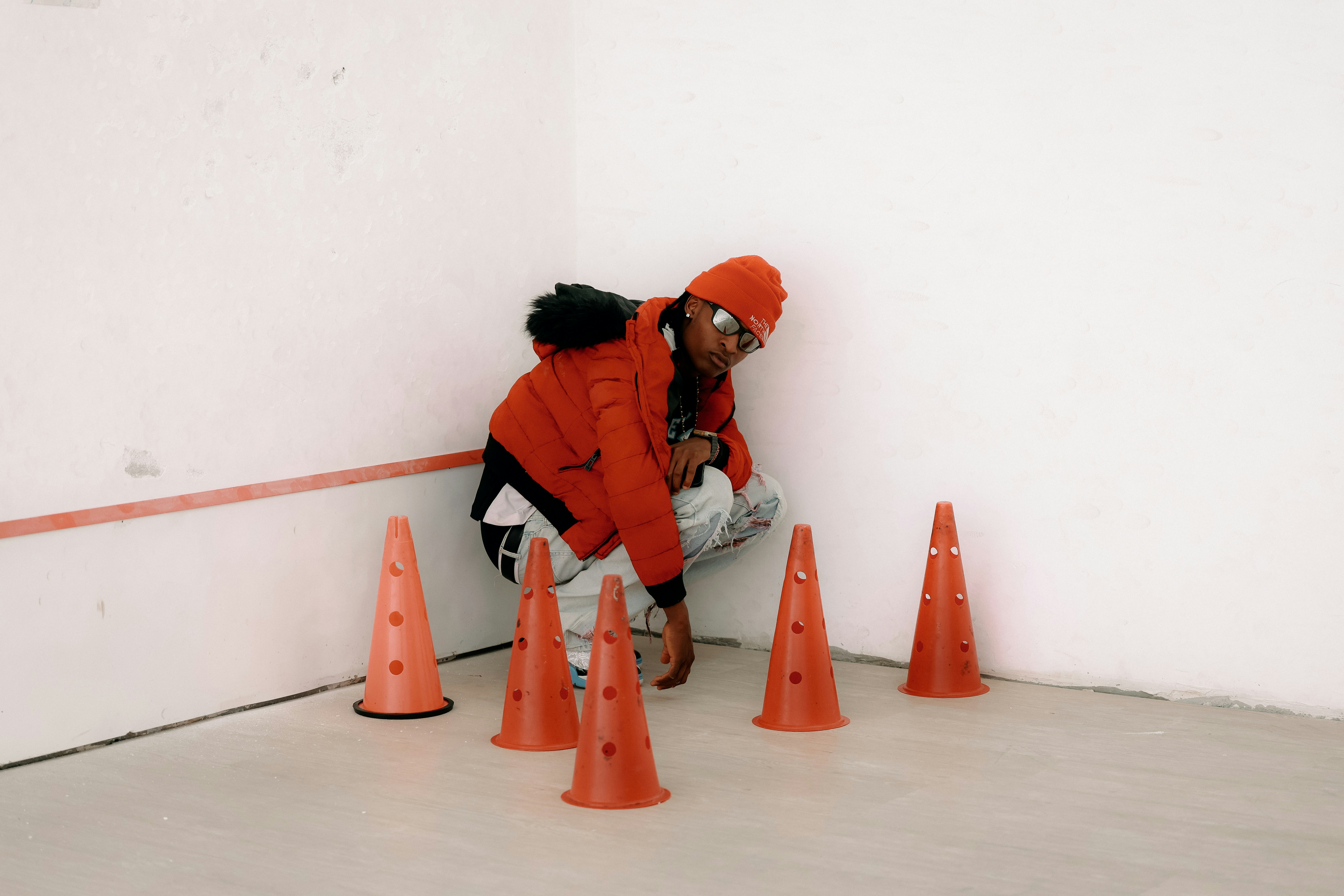 Person in orange jacket crouches near traffic cones.