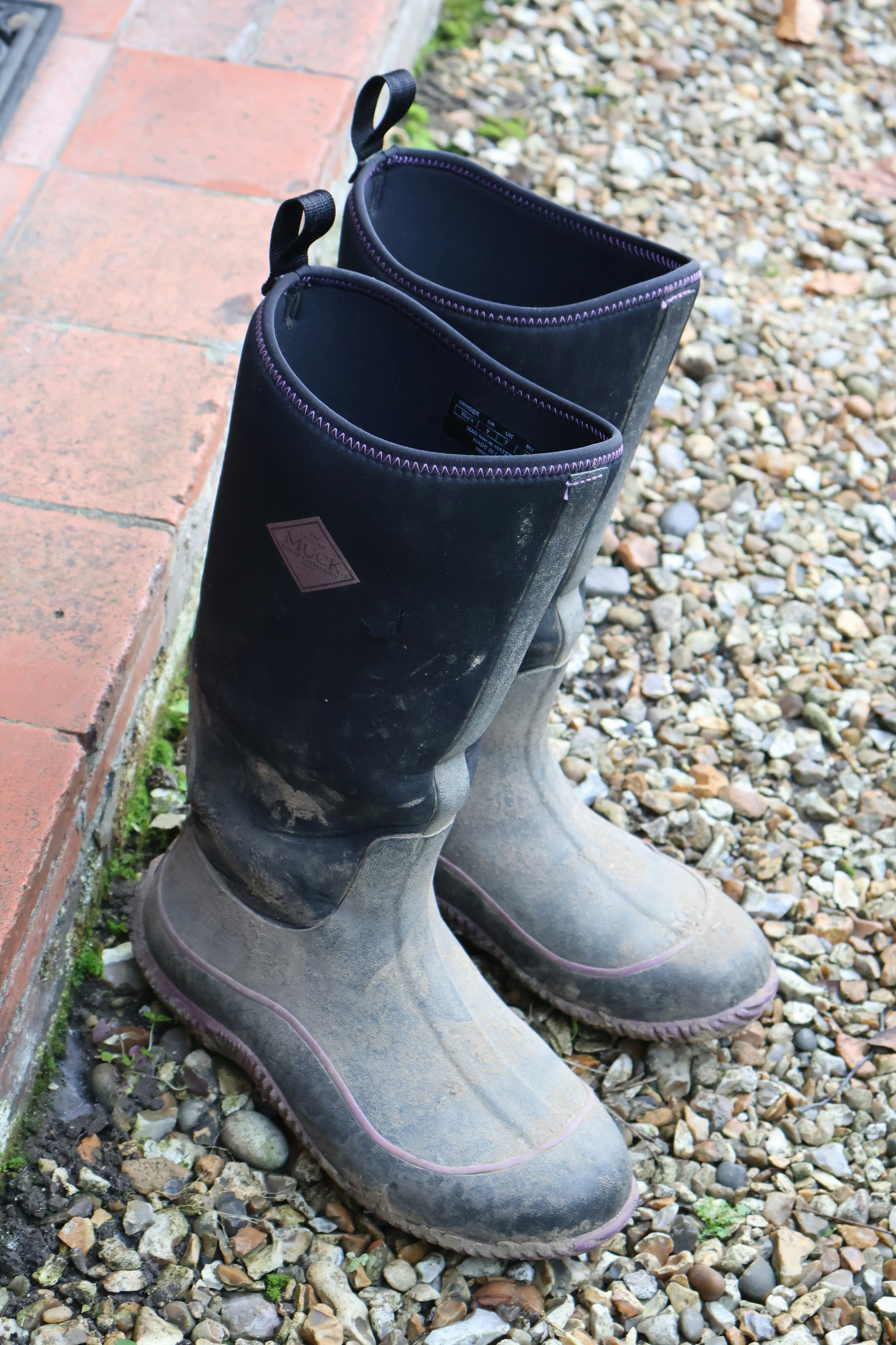 Pair of muddy black rubber boots on gravel.