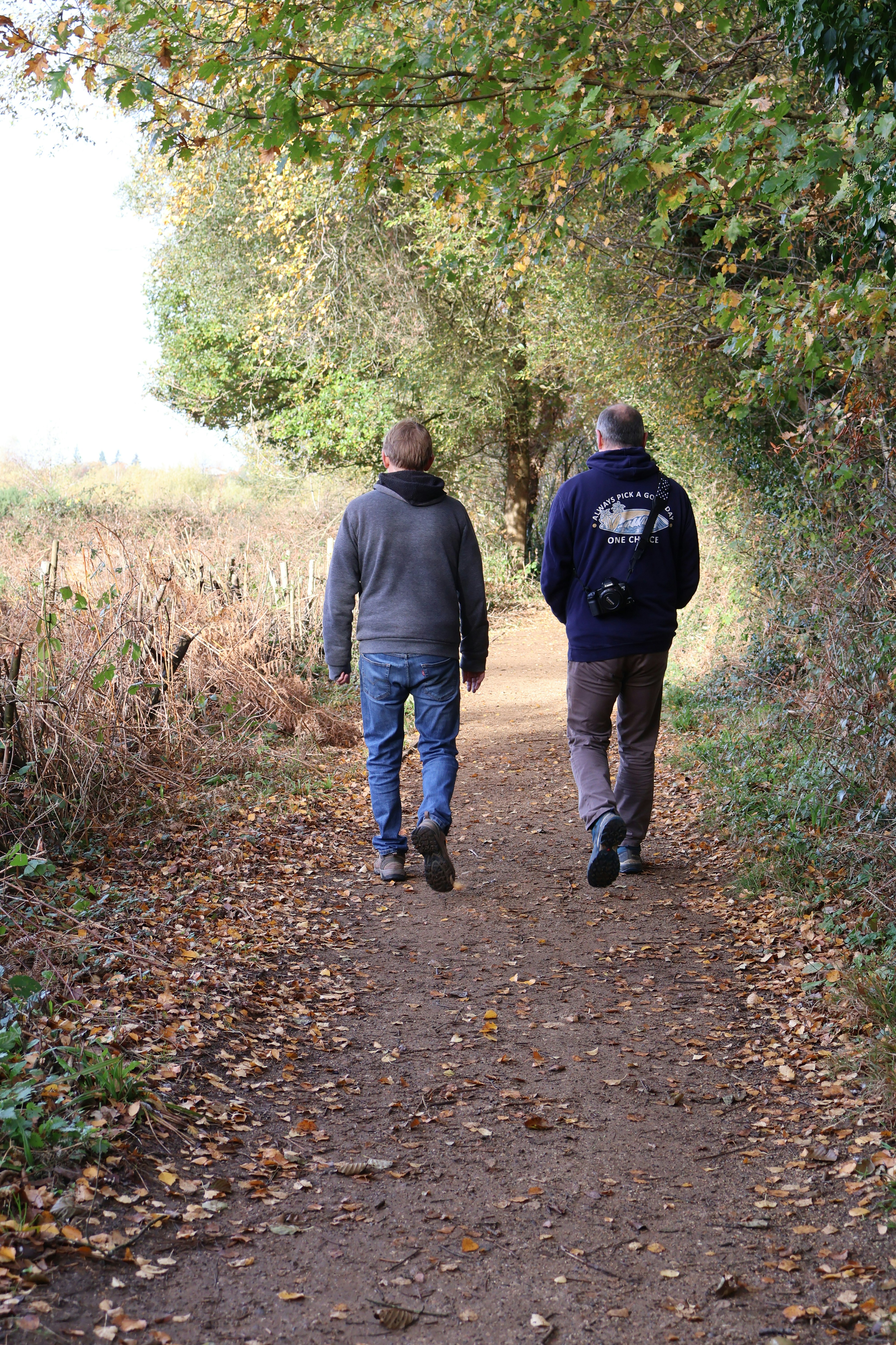 Two men walking down a leaf-covered path