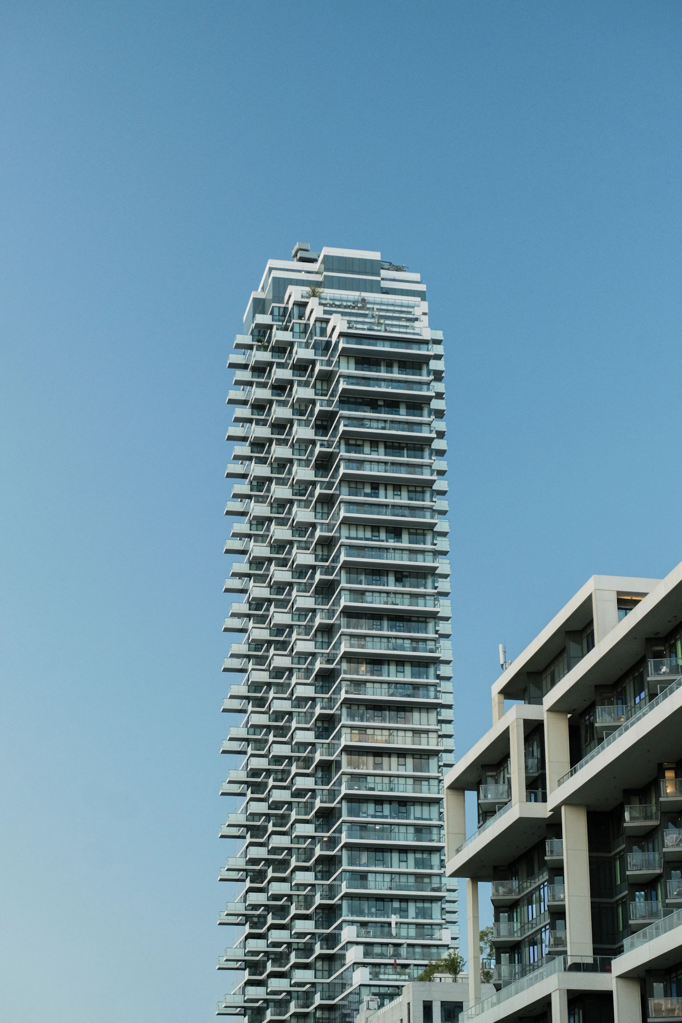 A tall residential condo tower with balconies against a clear blue Florida sky