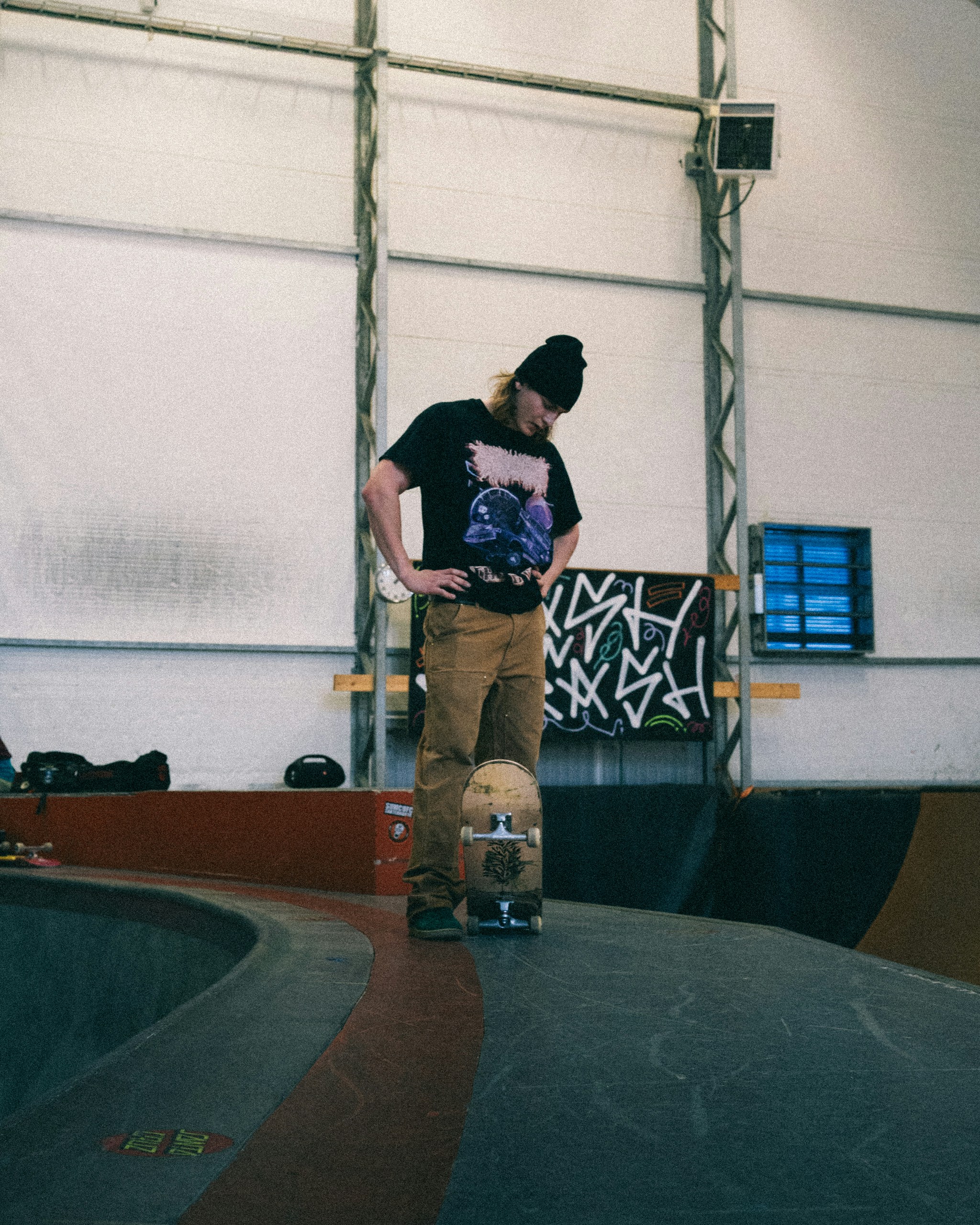 A person stands with a skateboard in a skatepark.