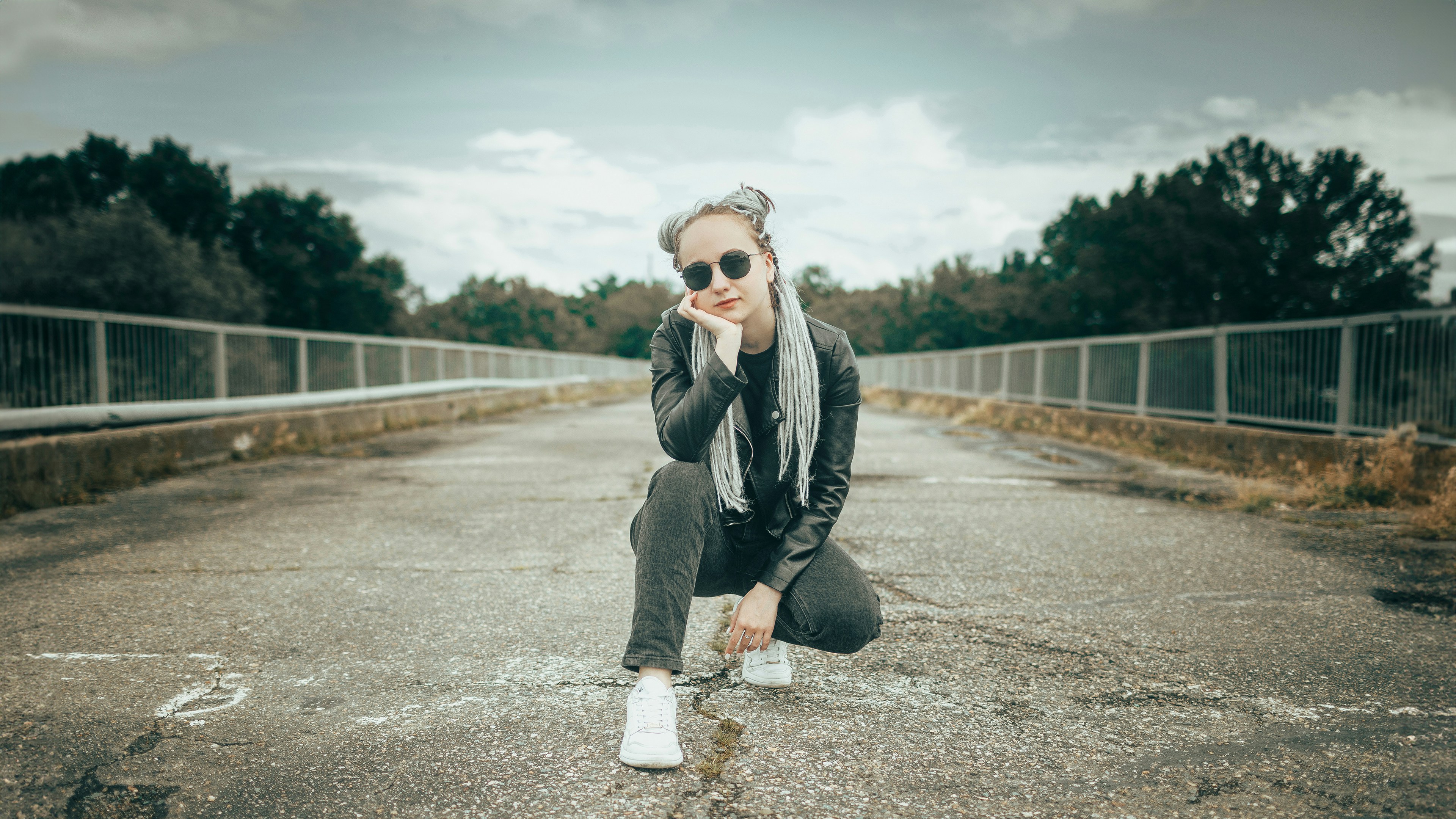 Woman crouching on an empty road with trees