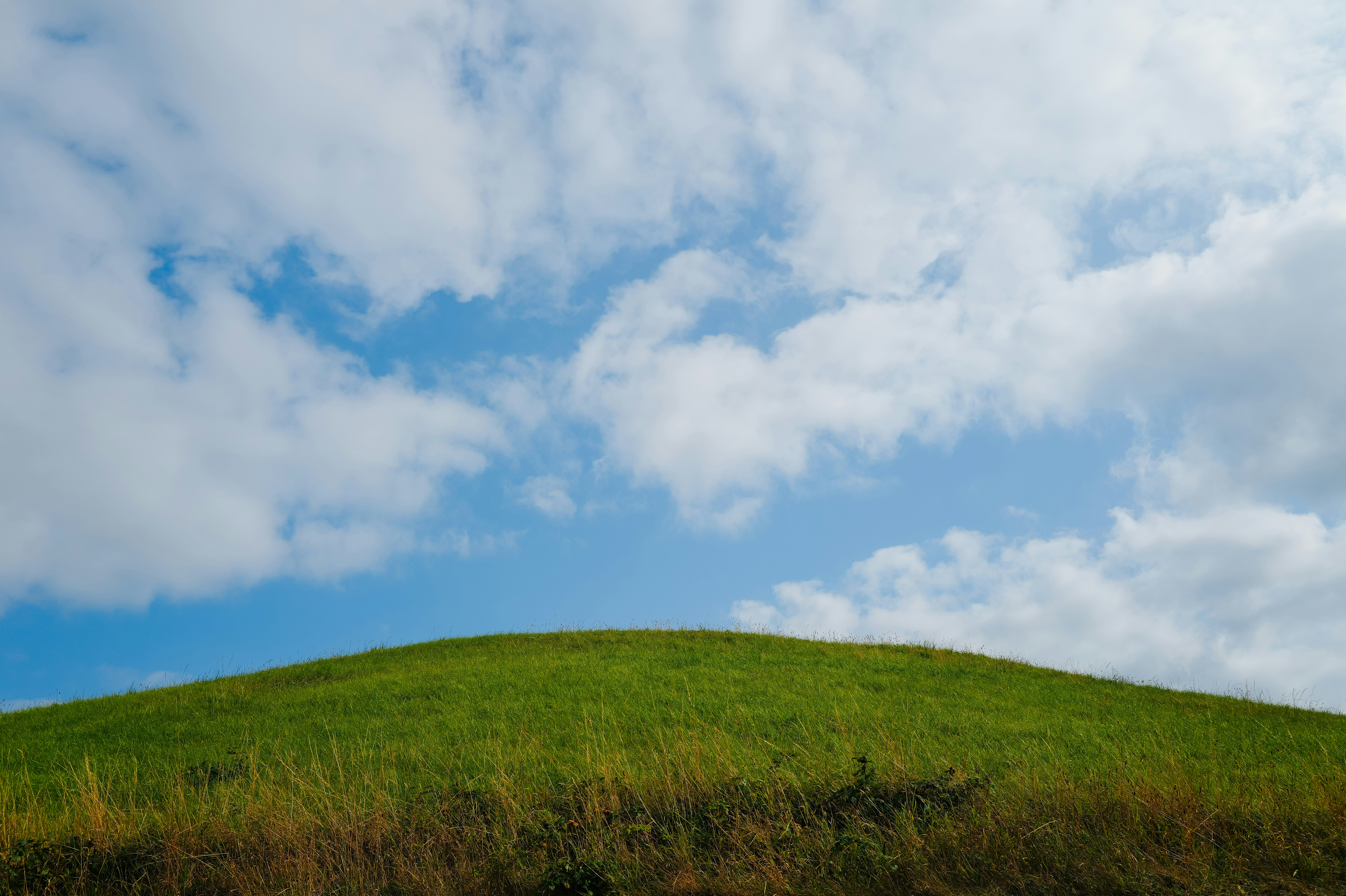 Colina verde bajo un cielo azul con nubes