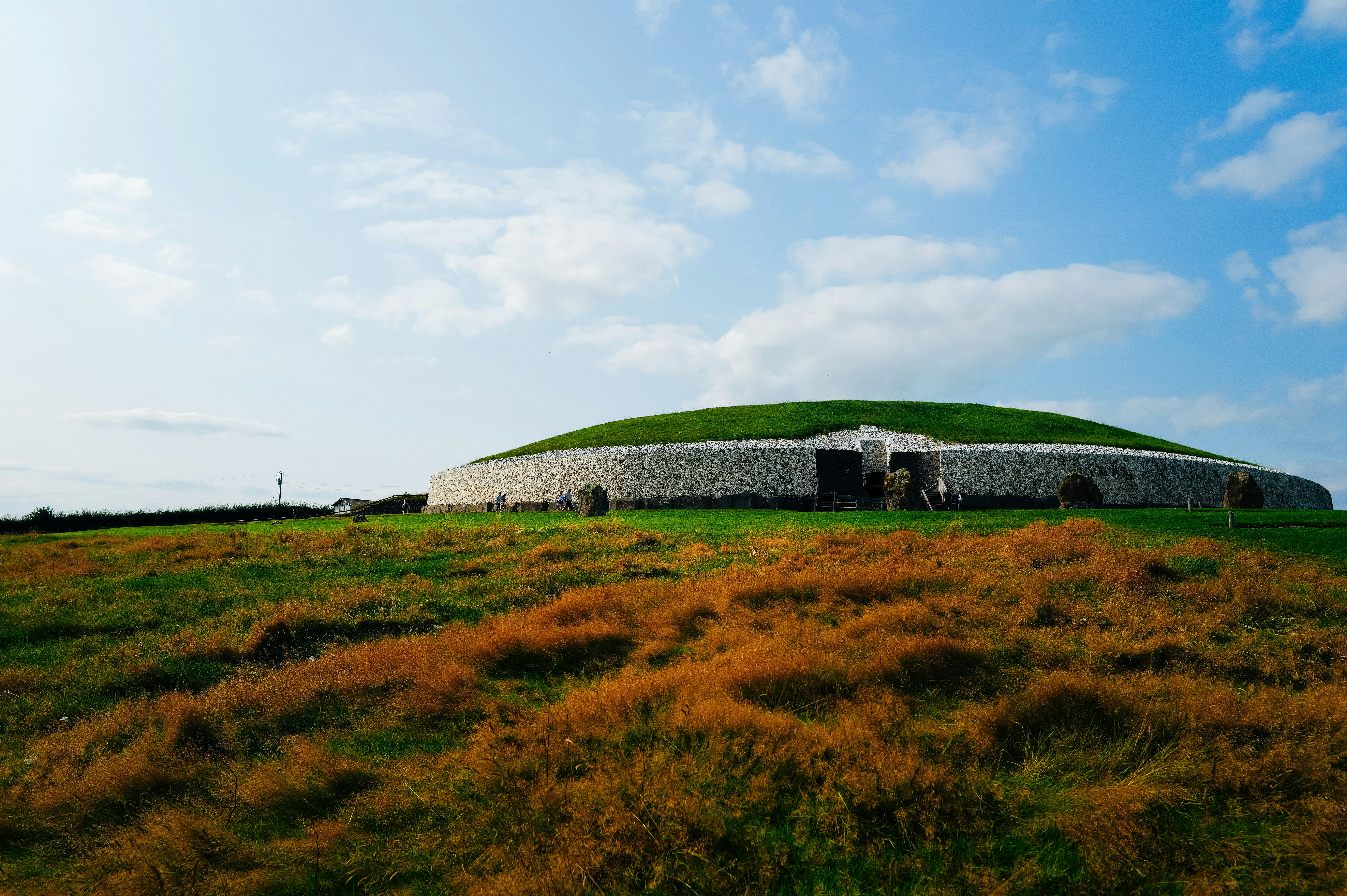 Ancient mound structure with green grass and blue sky.