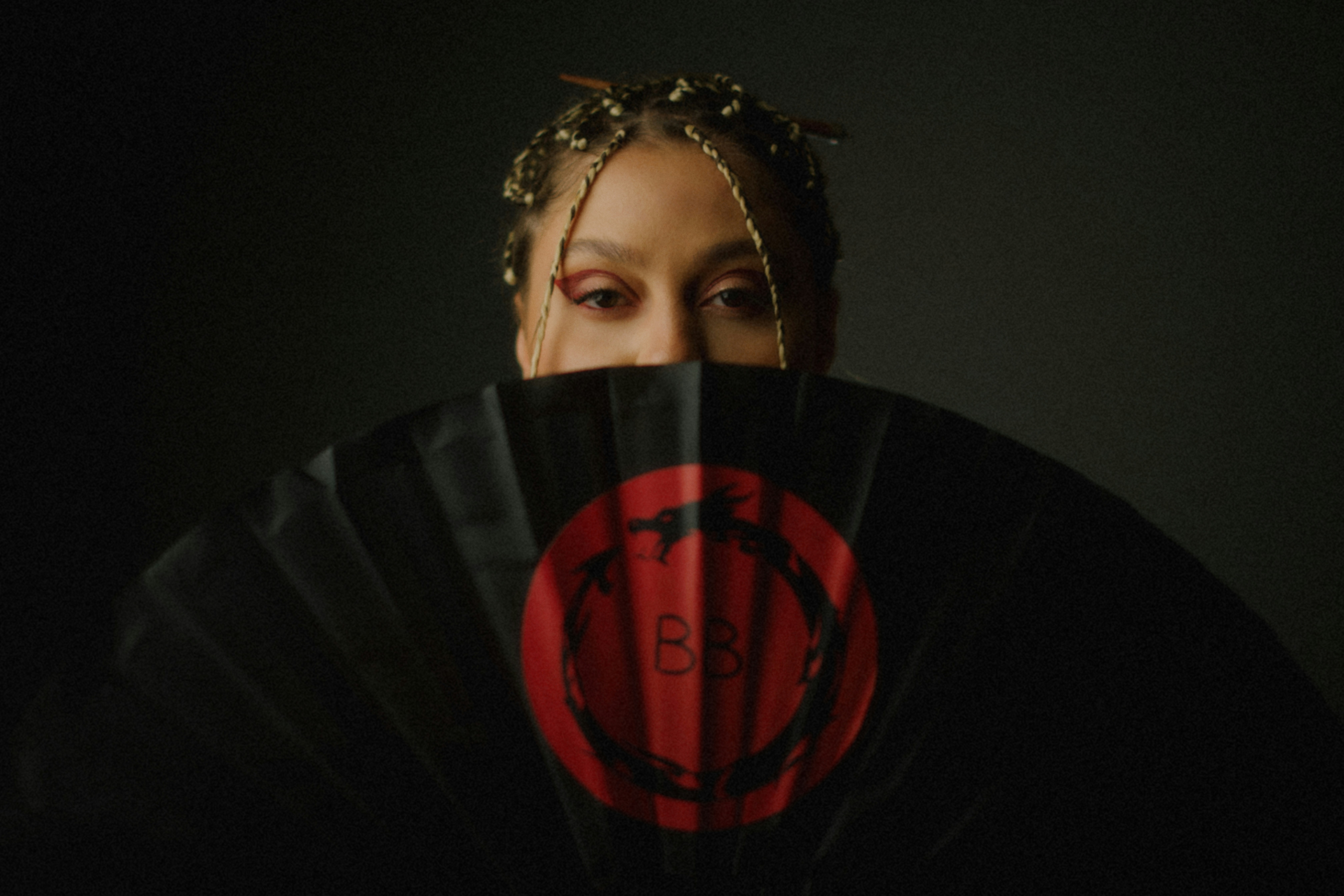 Woman with braided hair hides face behind fan
