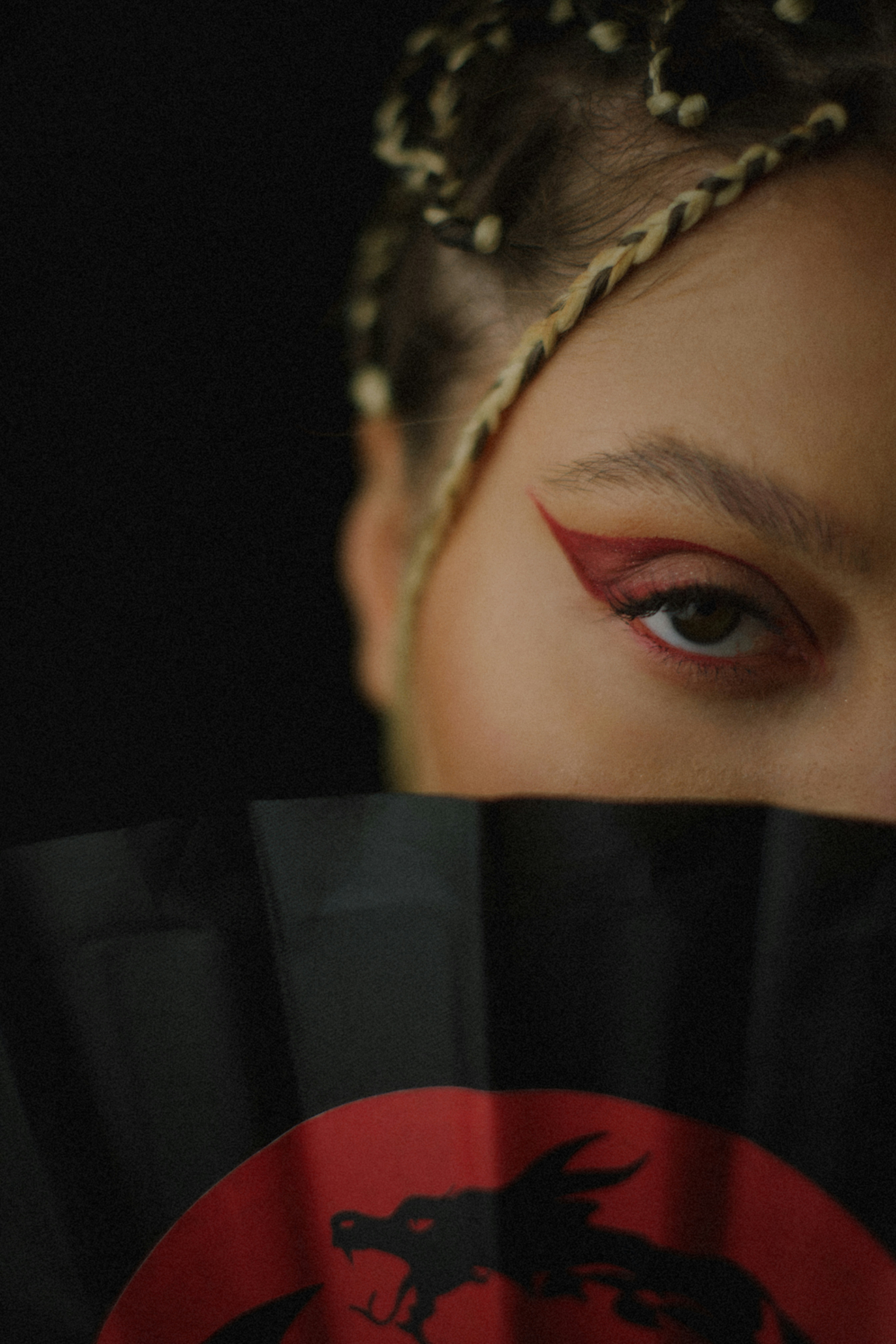Woman with dramatic eye makeup and braided hair holds fan