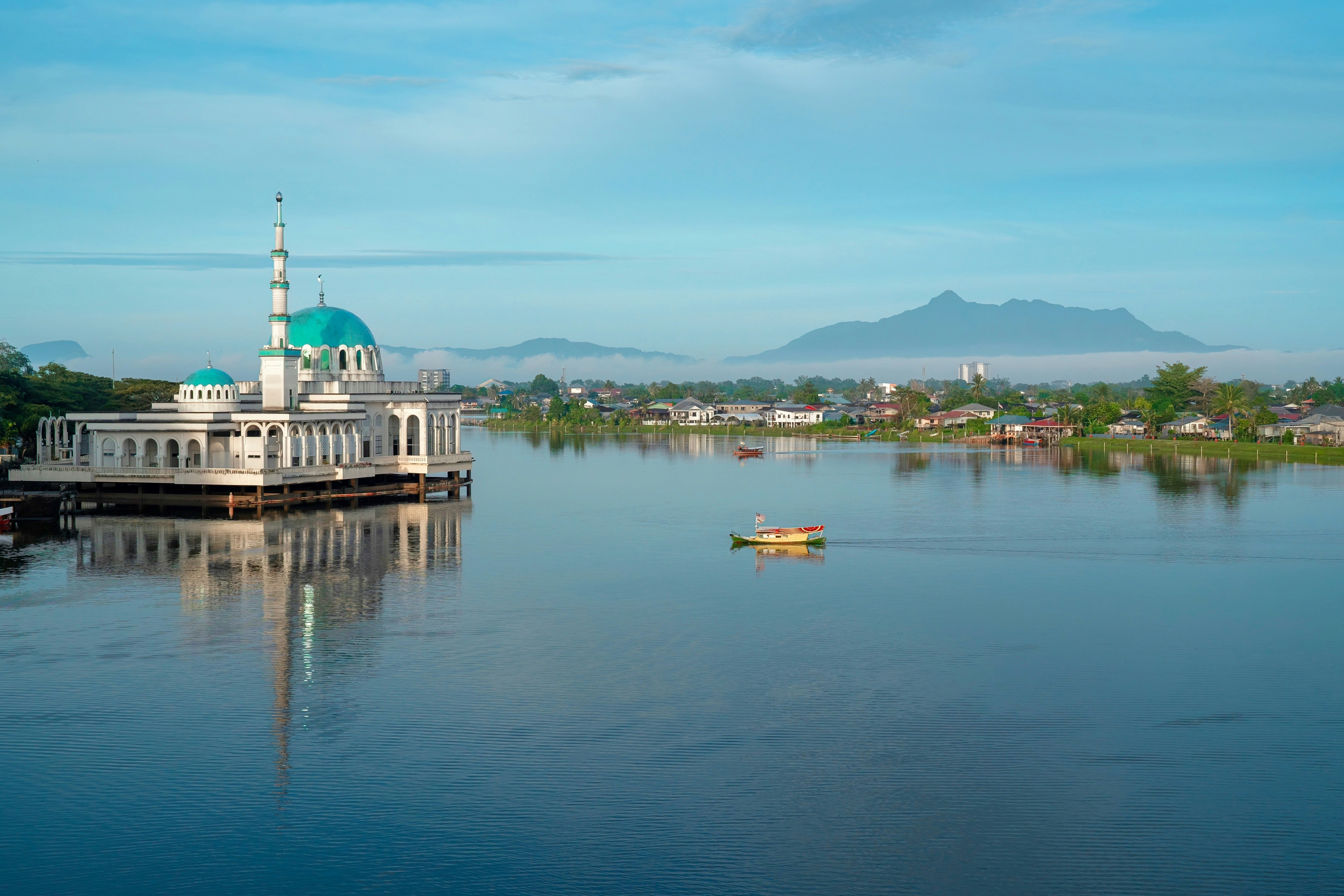 Mosque on the water with a boat and mountains.