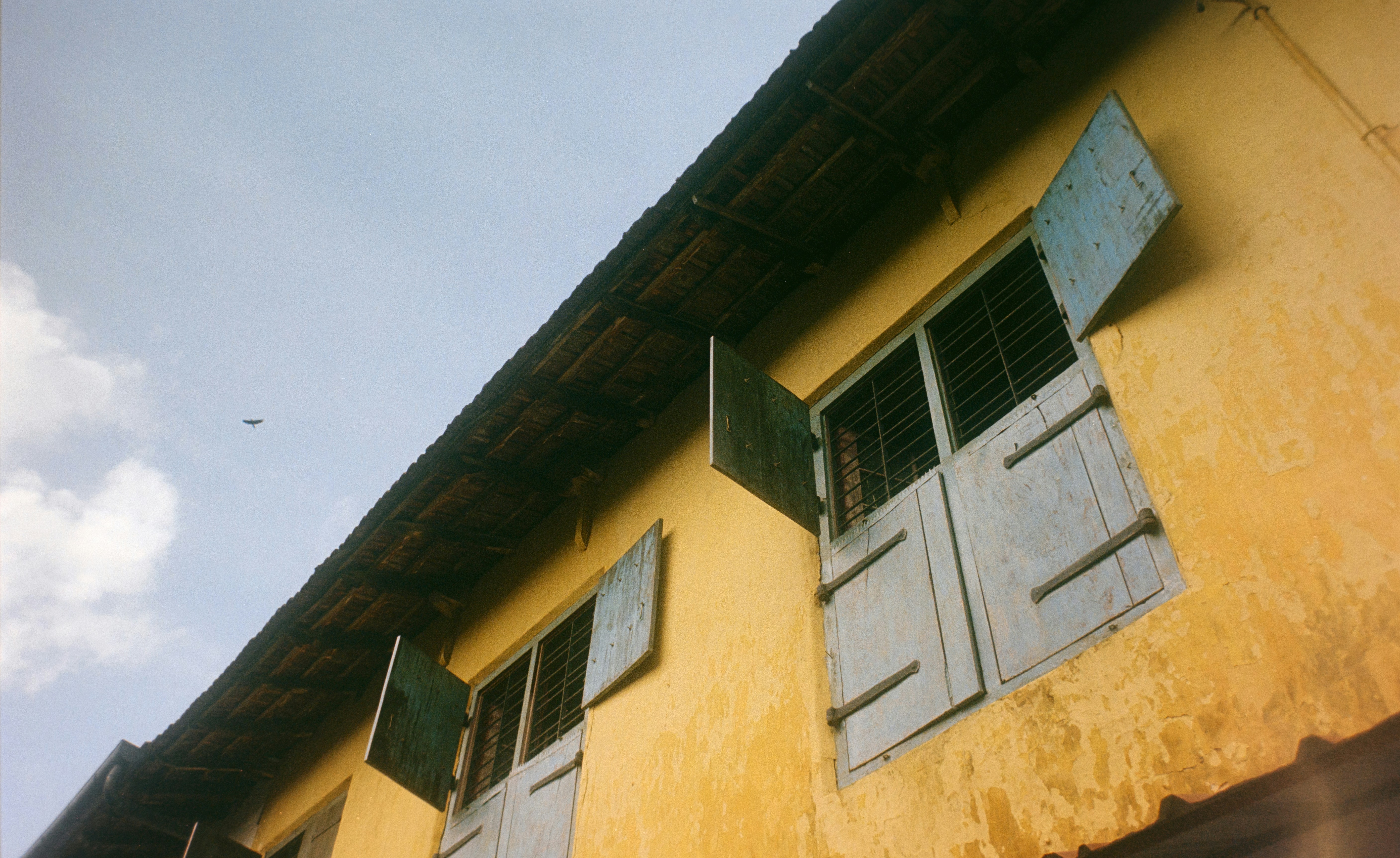 Yellow building with open blue shutters under a cloudy sky