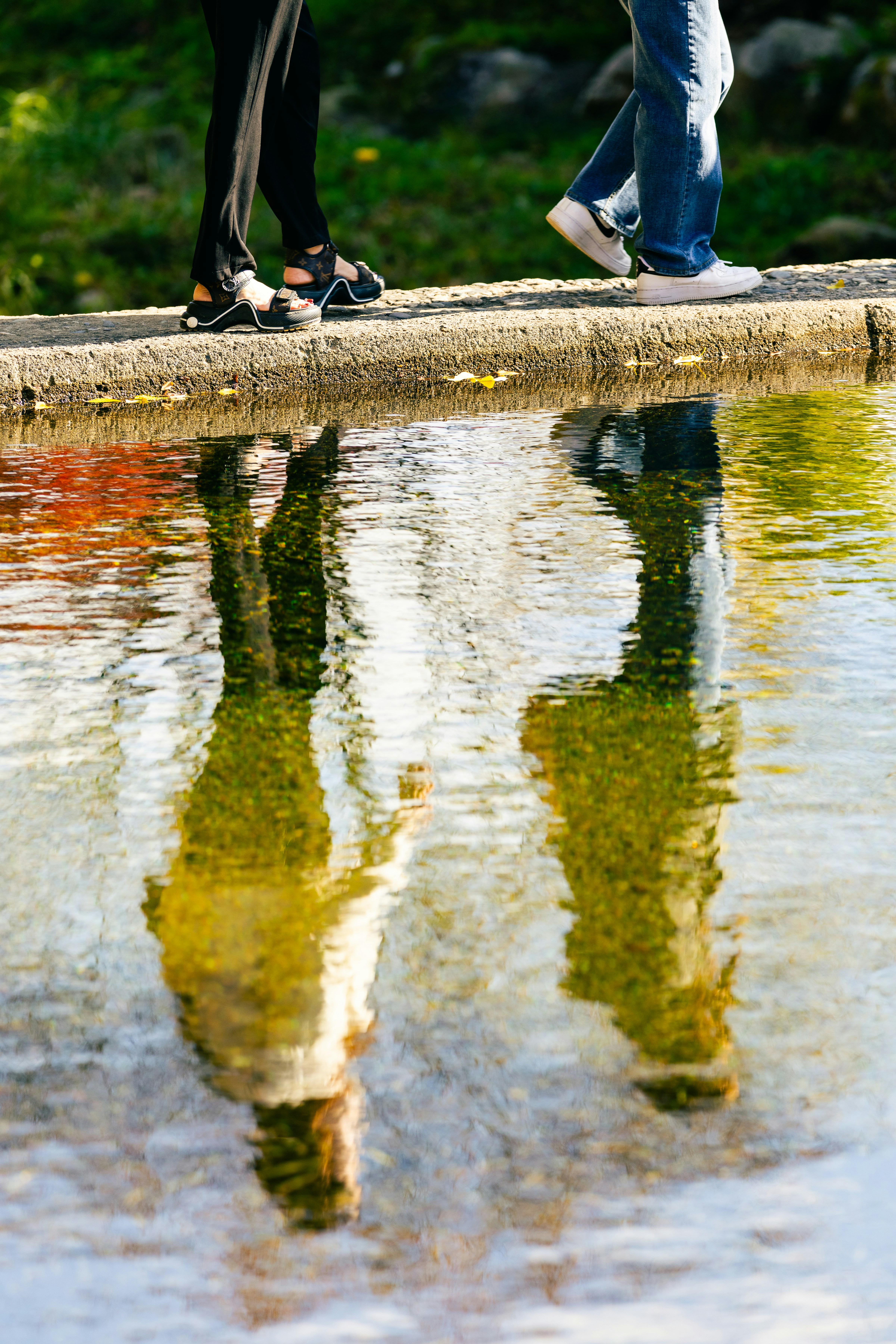 Two people walking beside water with reflections.