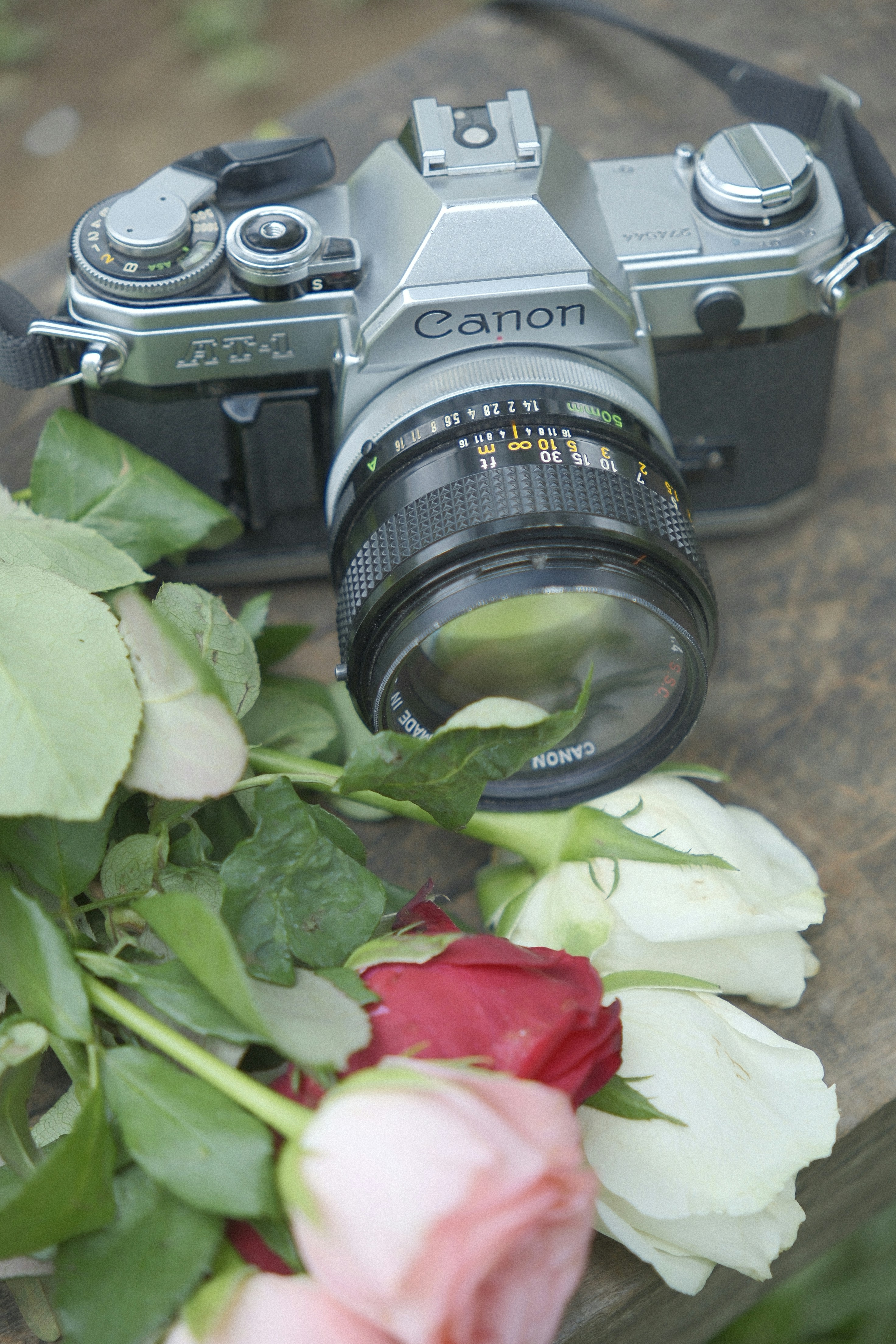 Vintage canon camera with roses on wooden surface